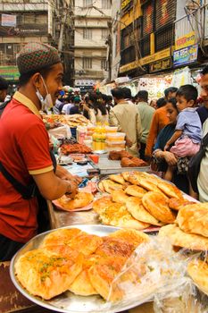 Bustling street market in Dhaka with vendor selling traditional bread and locals shopping, capturing cultural vibrance.