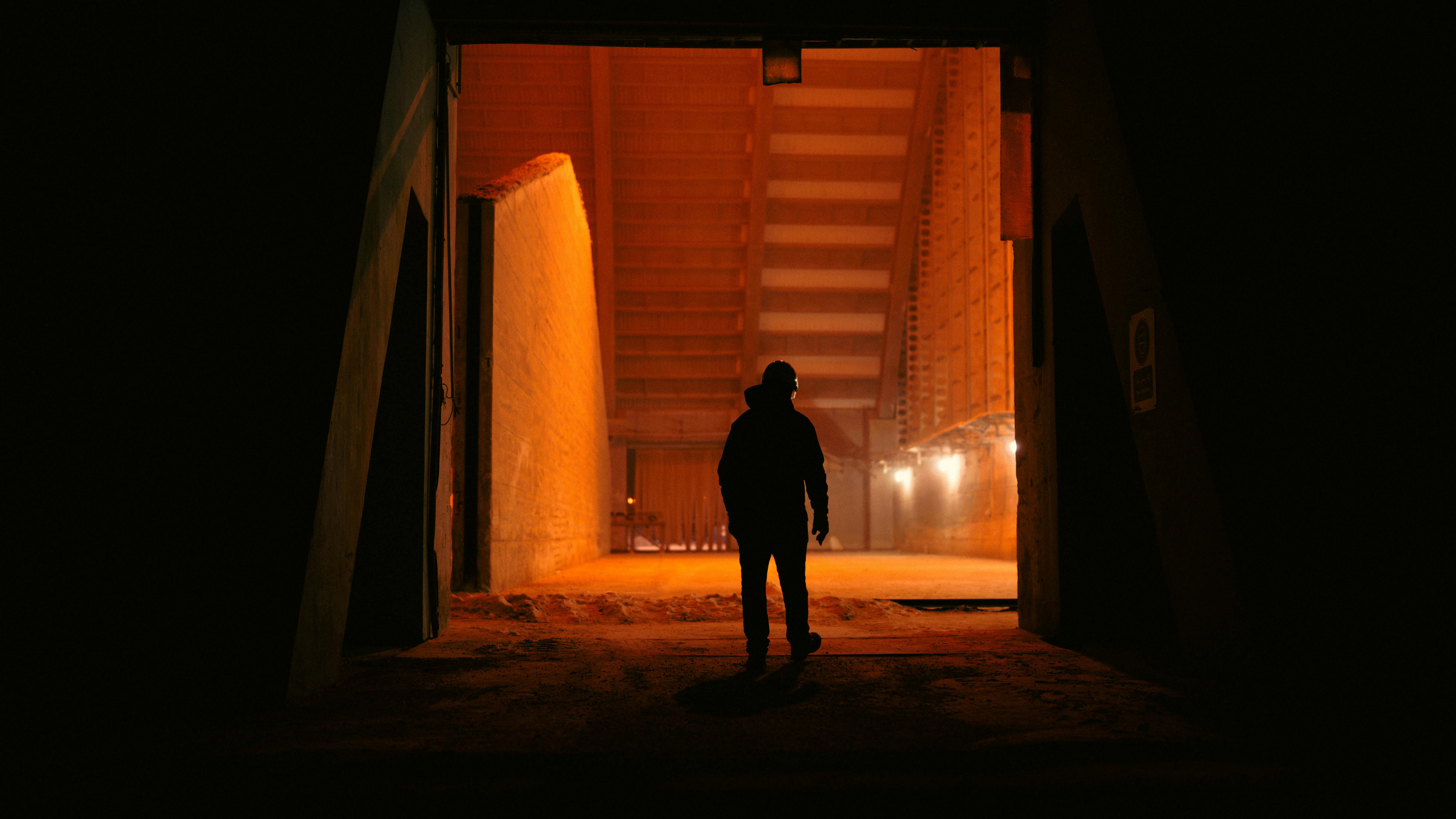 Gratuit Silueta unei persoane se conturează pe fundalul unui interior industrial puternic luminat, creând un contrast dramatic. Fotografie de stoc