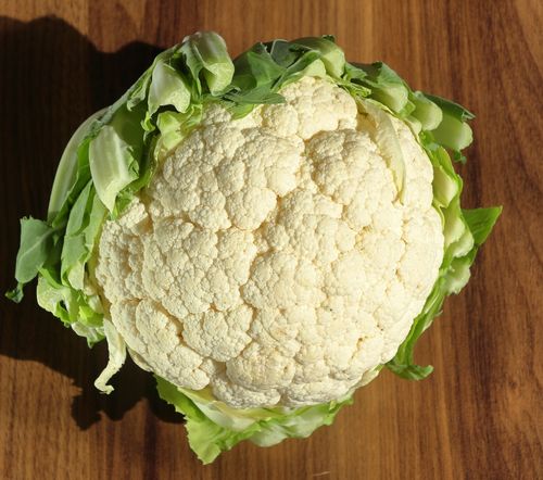 Free Top view of a fresh cauliflower head on a wooden surface, showcasing its texture and freshness. Stock Photo