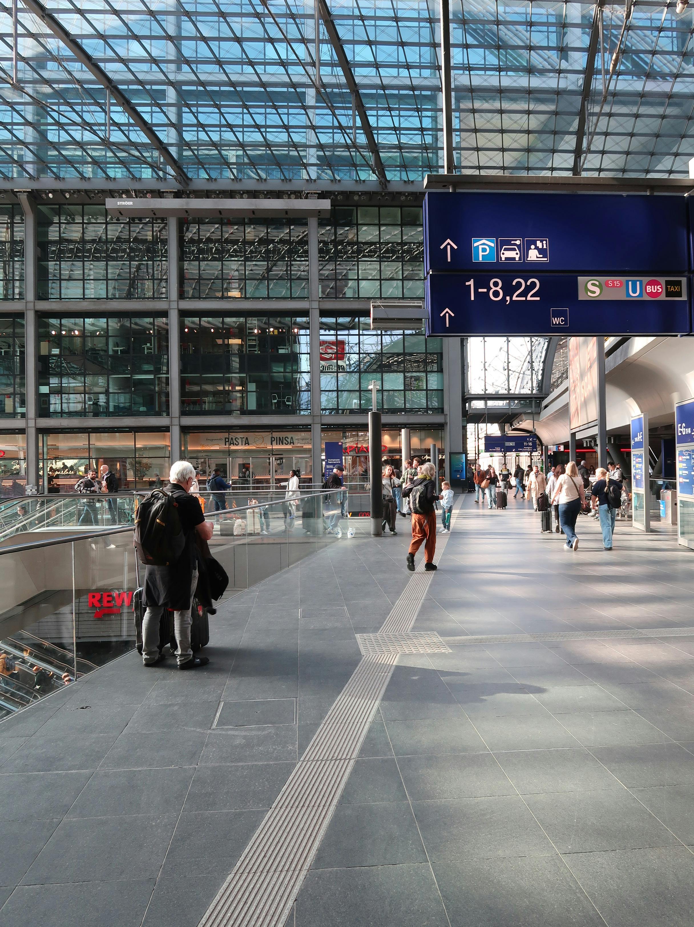 Gratis Una moderna e vivace stazione ferroviaria, animata da persone e segnaletica, che illustra la vita urbana legata ai viaggi. Foto a disposizione