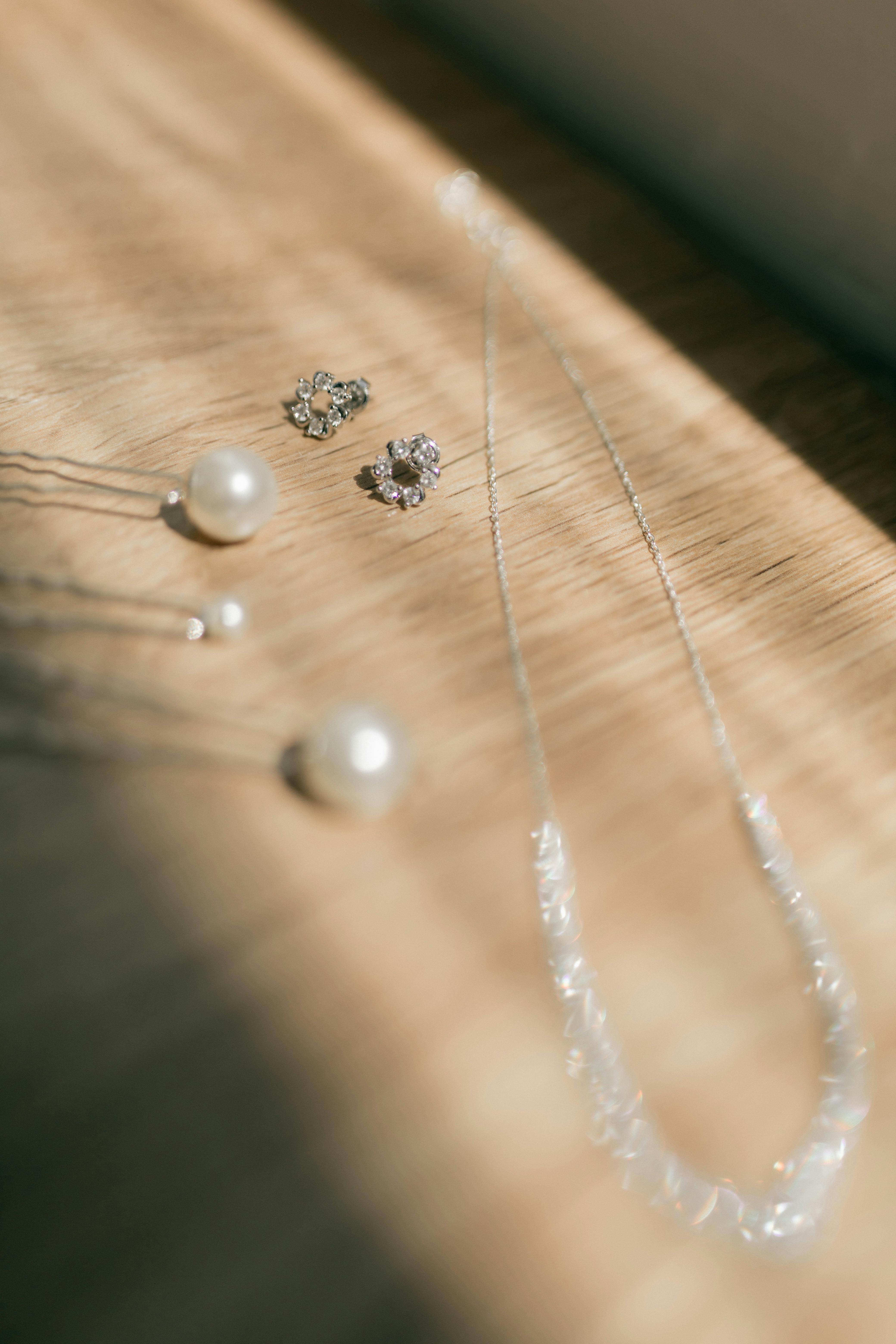 Gratis Elegante esposizione di orecchini di perle e gioielli con diamanti su una superficie in legno con illuminazione soffusa. Foto a disposizione