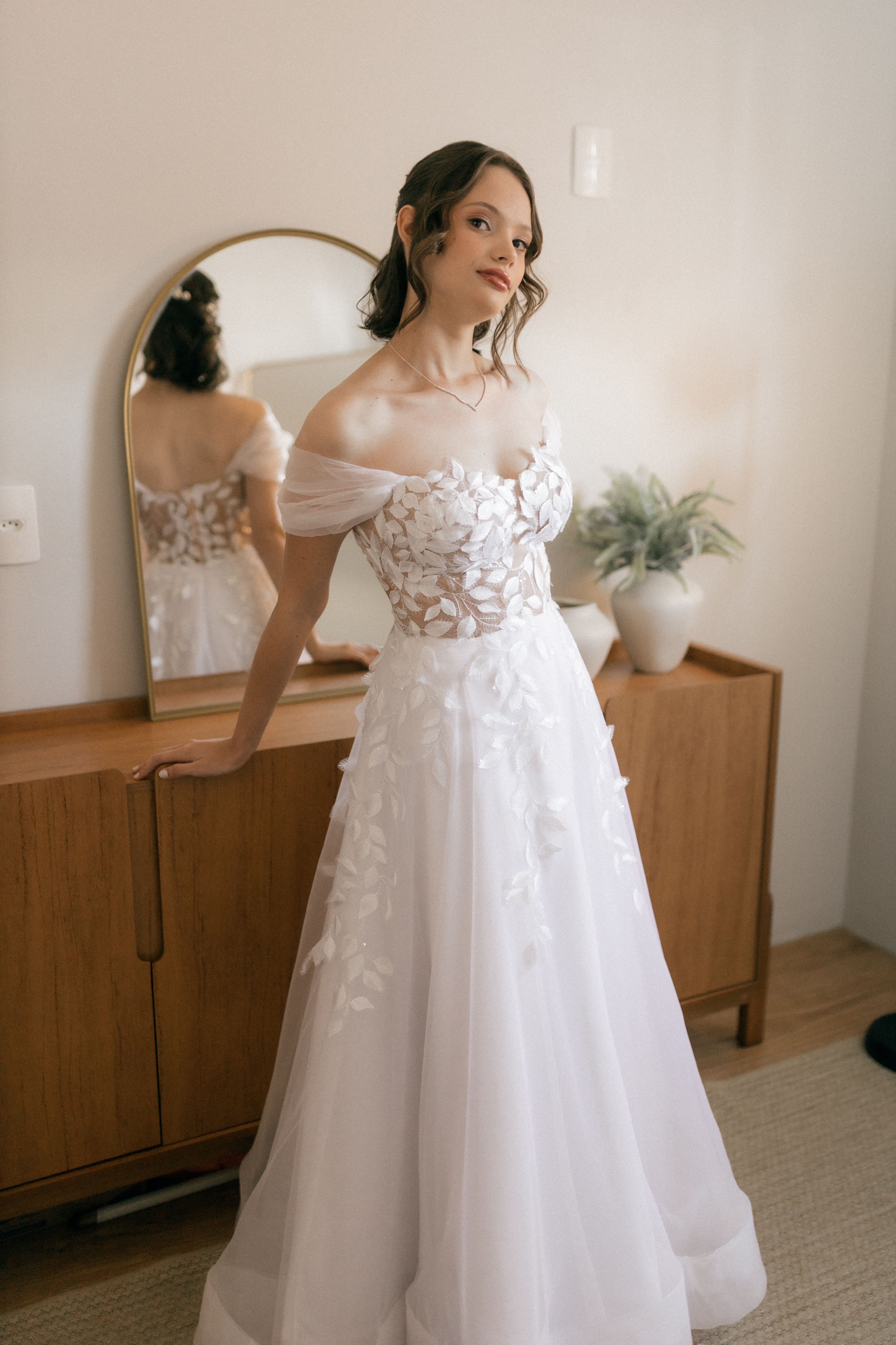 A beautiful bride in a stylish white gown poses indoors, showcasing bridal elegance and charm.