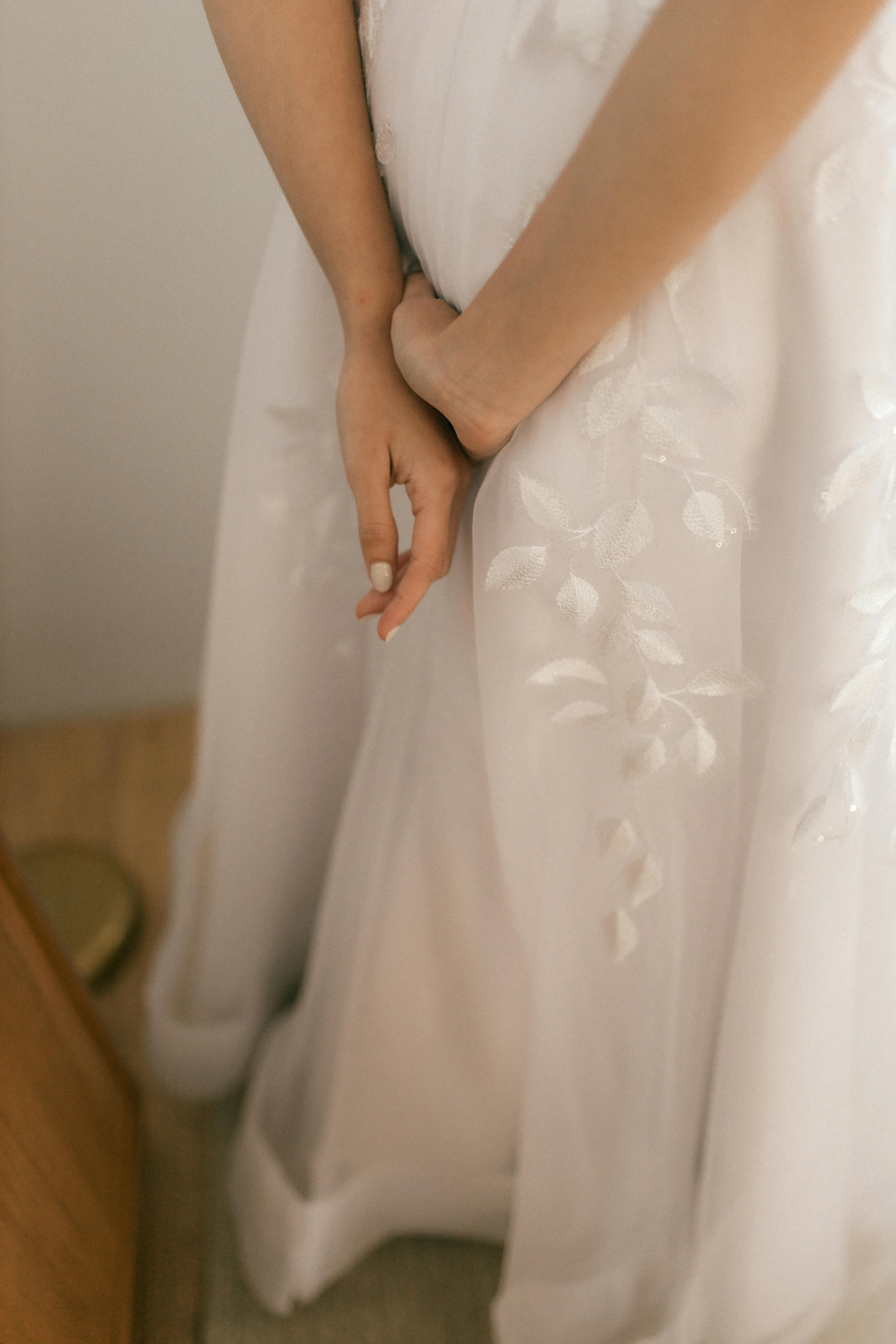 無料 花柄があしらわれた白いウェディングドレスを着た花嫁が、優雅に手をつないでいるクローズアップ写真。 写真素材