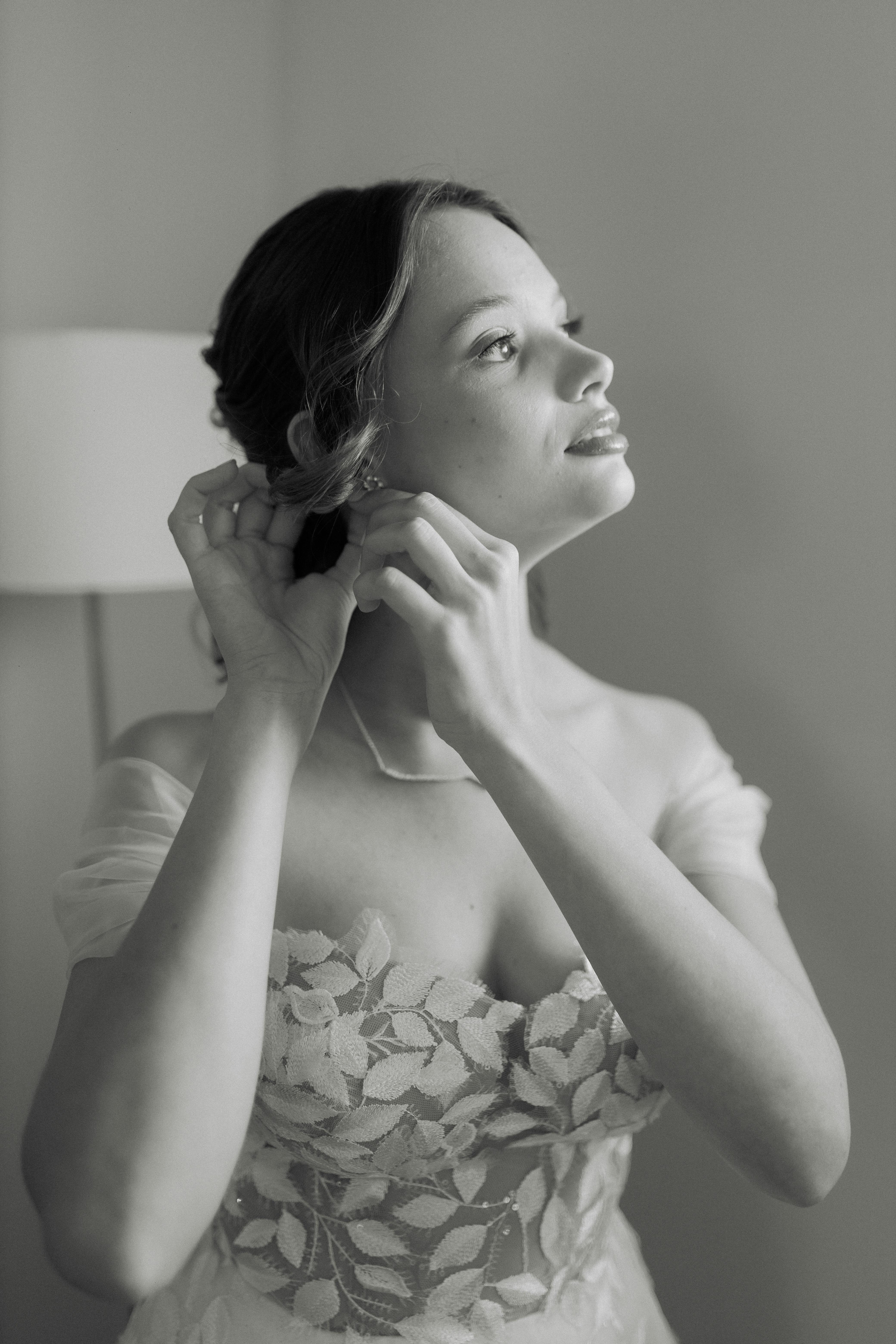 Gratuit Portrait en noir et blanc d'une mariée ajustant ses boucles d'oreilles dans une élégante robe de mariée en dentelle. Photos