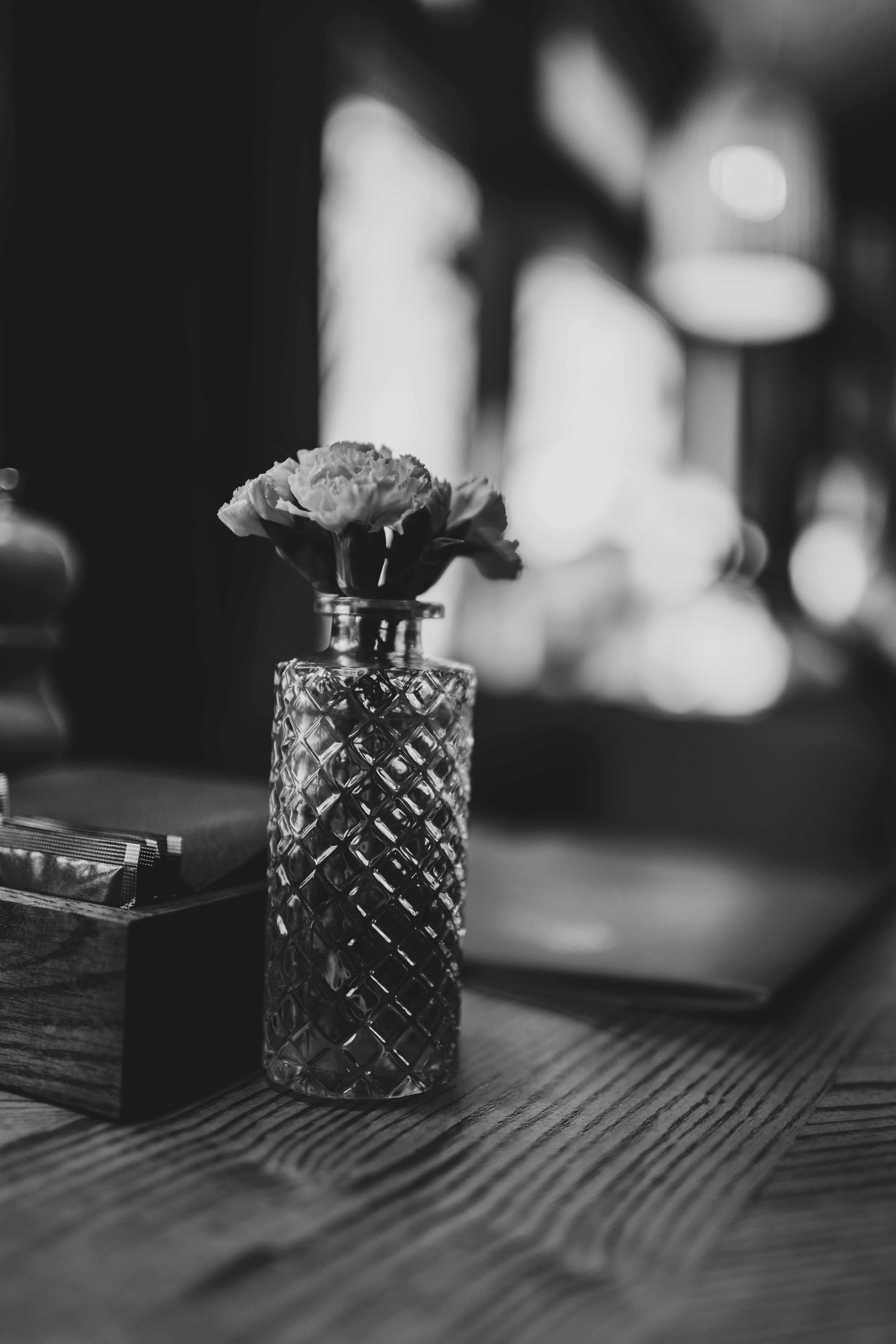 Gratis Una fotografia in bianco e nero di un garofano in un vaso di vetro lavorato su un tavolo di legno. Foto a disposizione