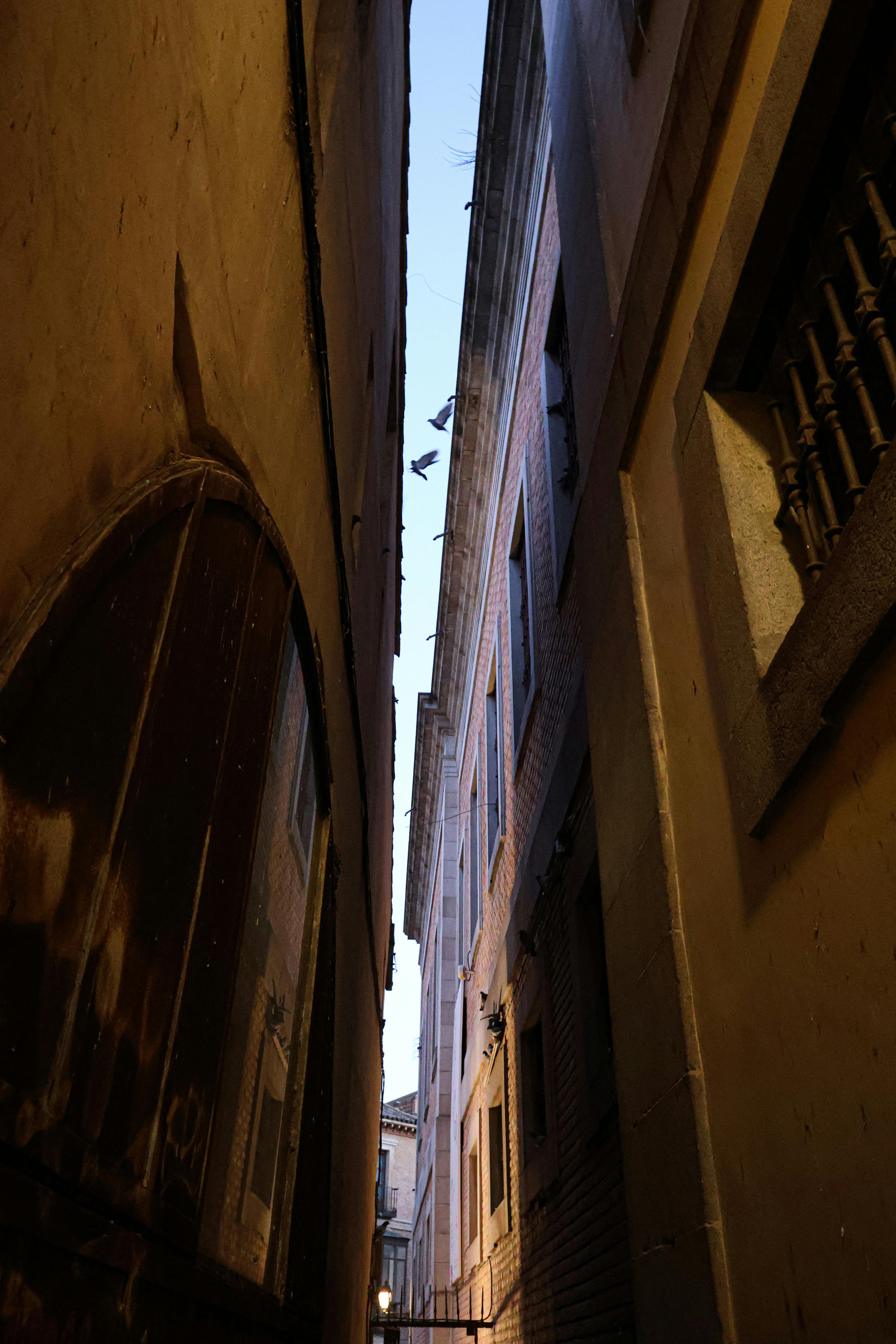 無料 スペインのトレドにある、夕暮れ時に撮影された狭い路地。古典的な建築様式が際立っている。 写真素材