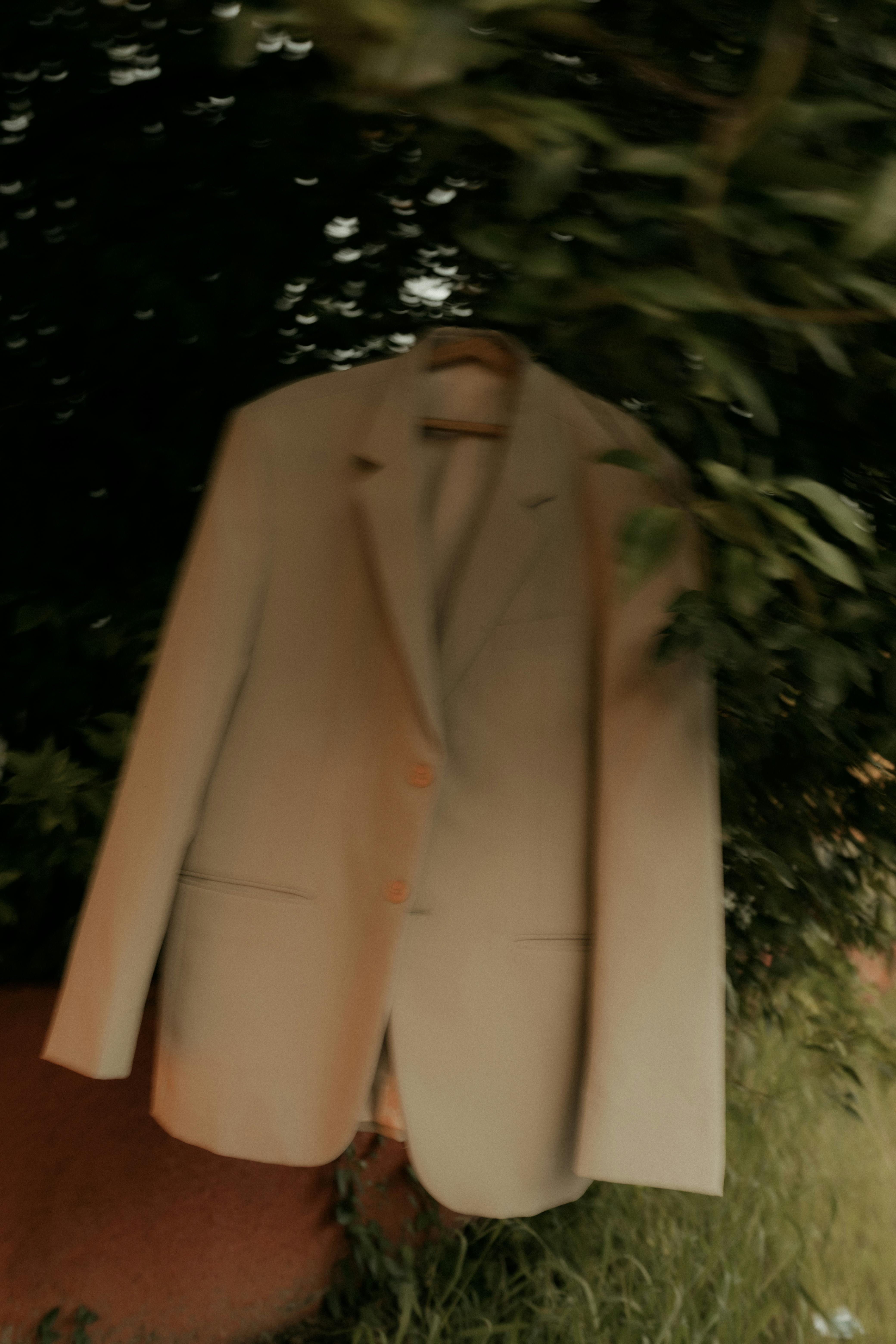 Free A beige suit jacket hanging on a tree branch in a garden setting. Stock Photo