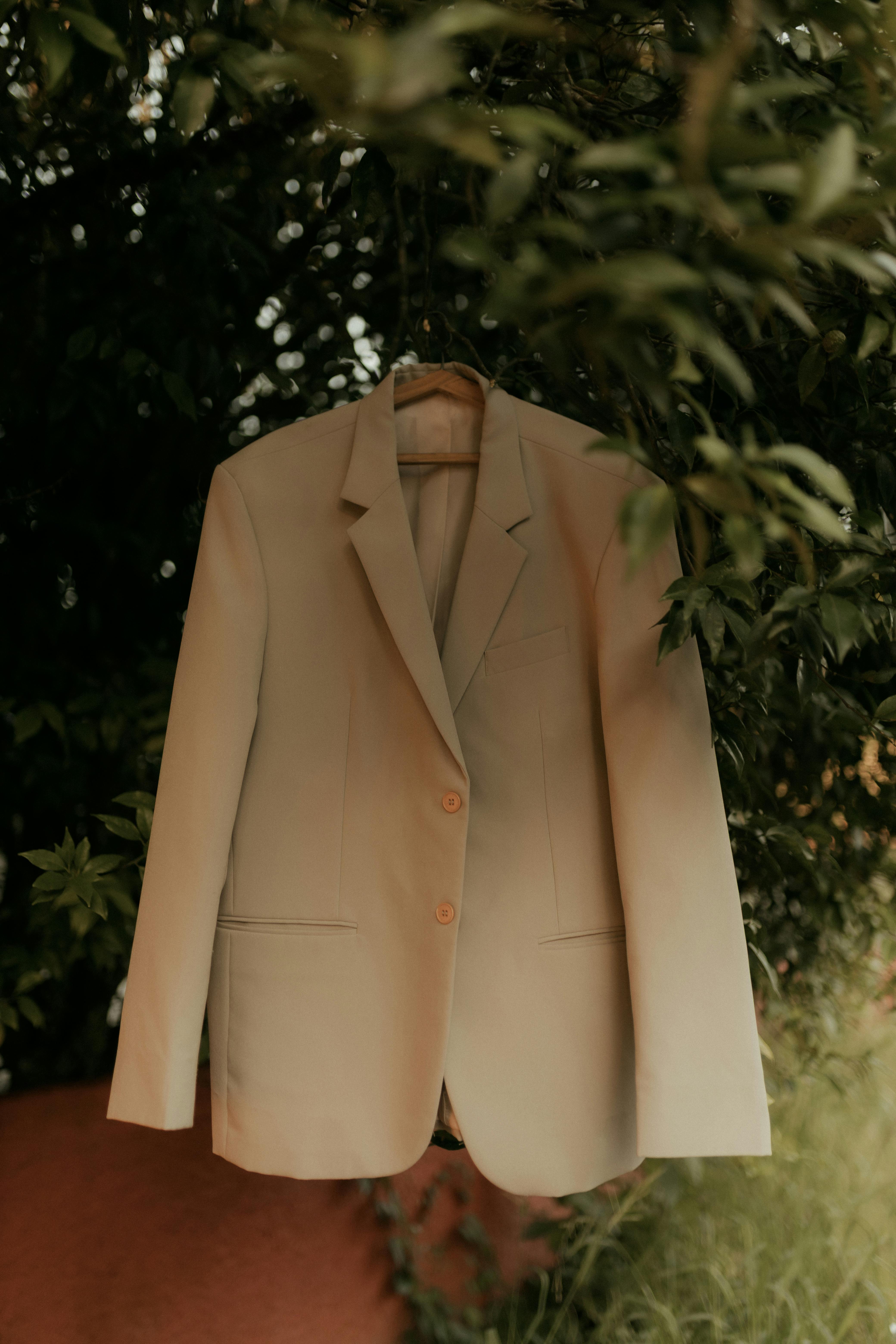 Kostenlos Ein eleganter beigefarbener Blazer hängt im Freien inmitten üppigen Grüns – perfekt für Modethemen. Stock-Foto