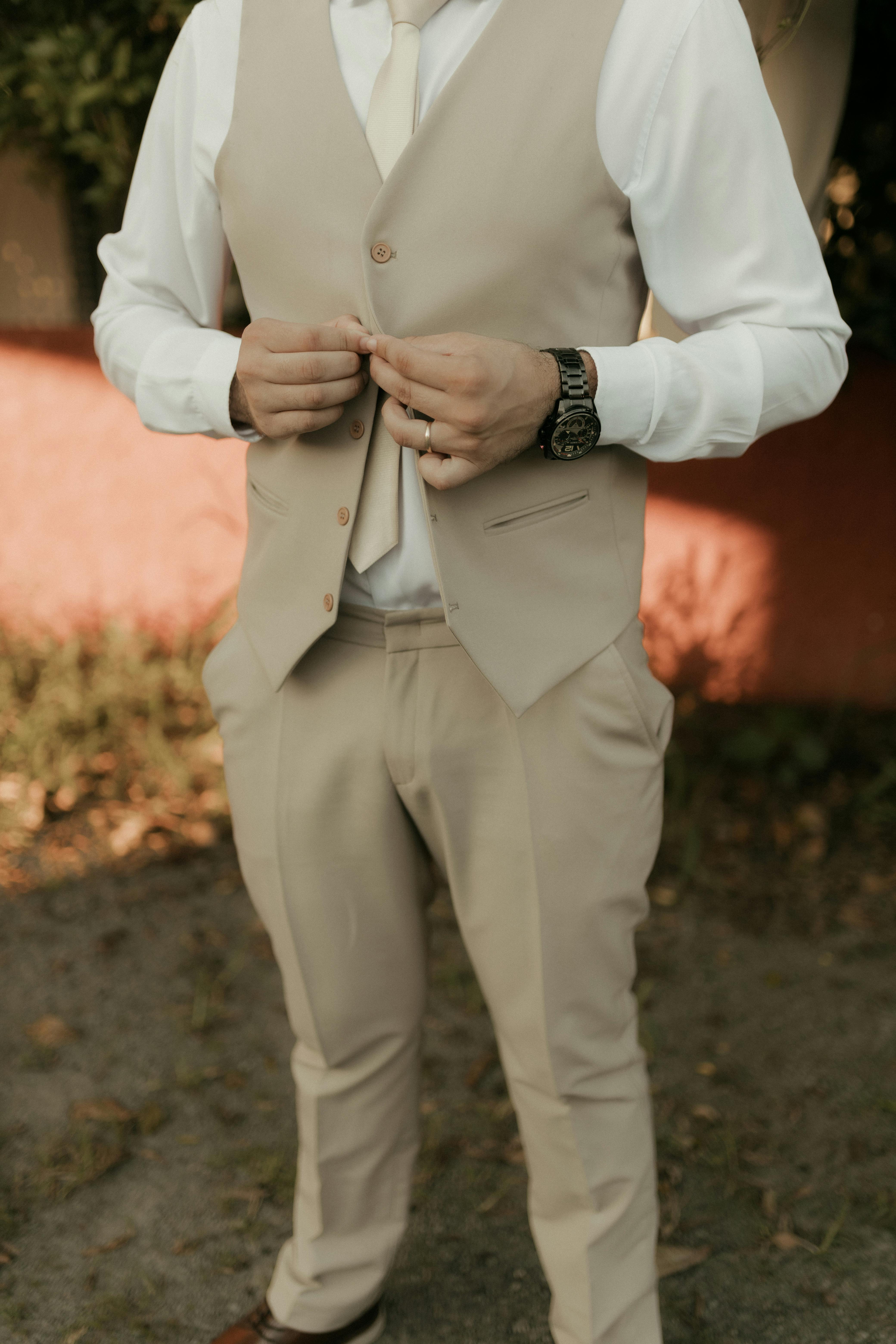 Gratis En mann i beige dress retter på vesten sin utendørs og forbereder seg til et arrangement. Arkivbilde