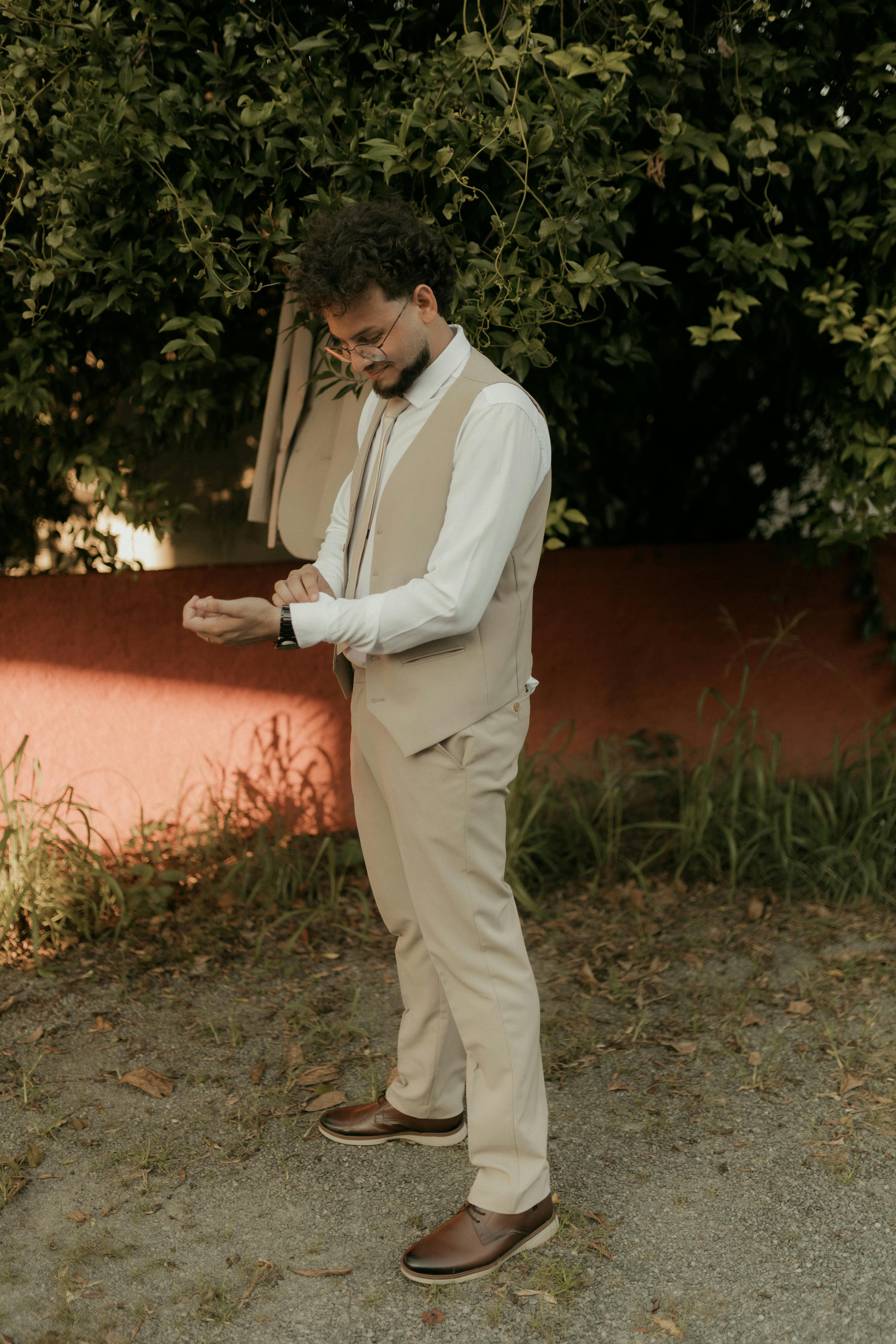 Gratuit Un homme en tenue de soirée ajuste ses poignets dans un cadre extérieur, dégageant une élégance naturelle. Photos