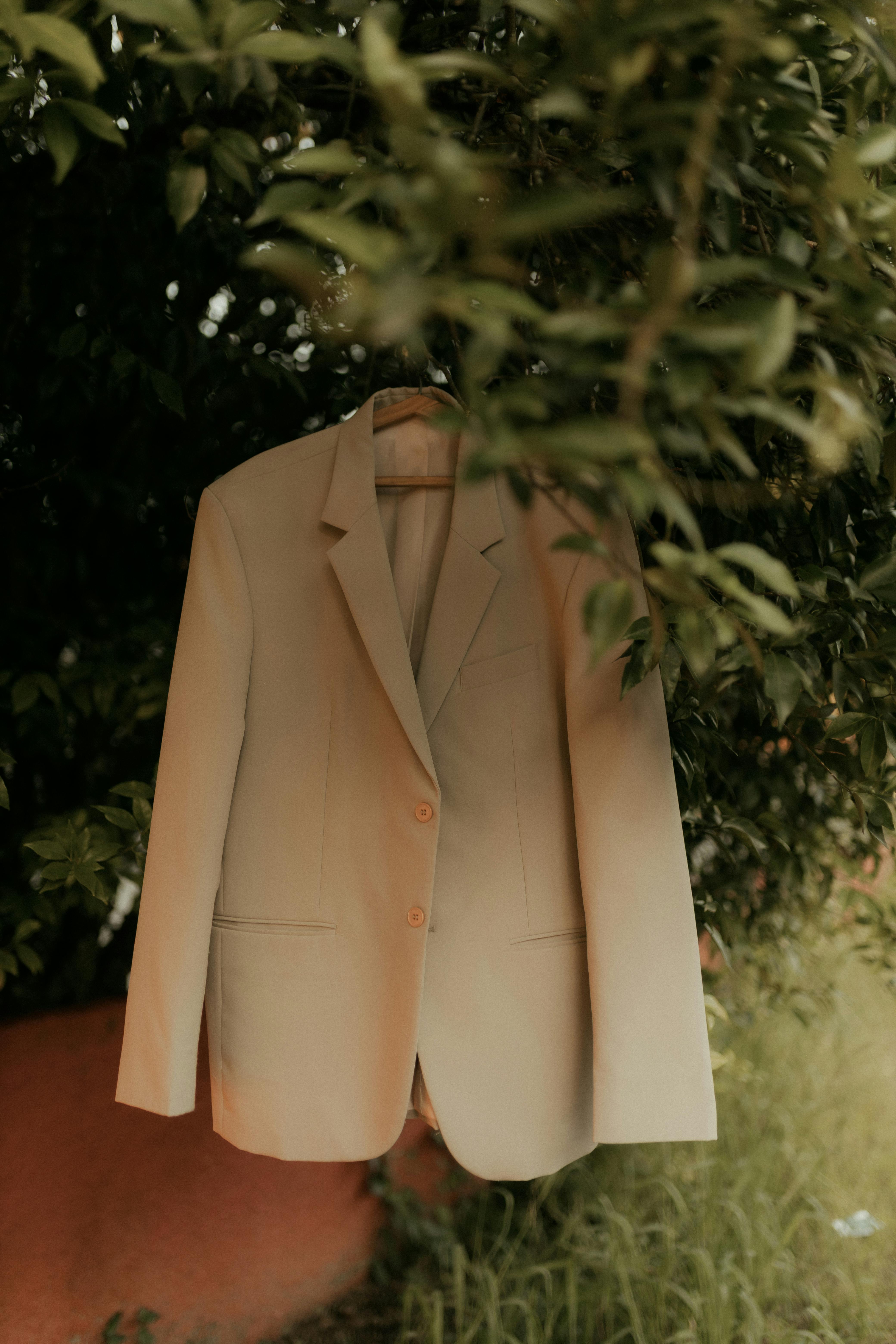 Free A stylish beige blazer hanging from a tree branch, presenting a unique natural backdrop. Stock Photo