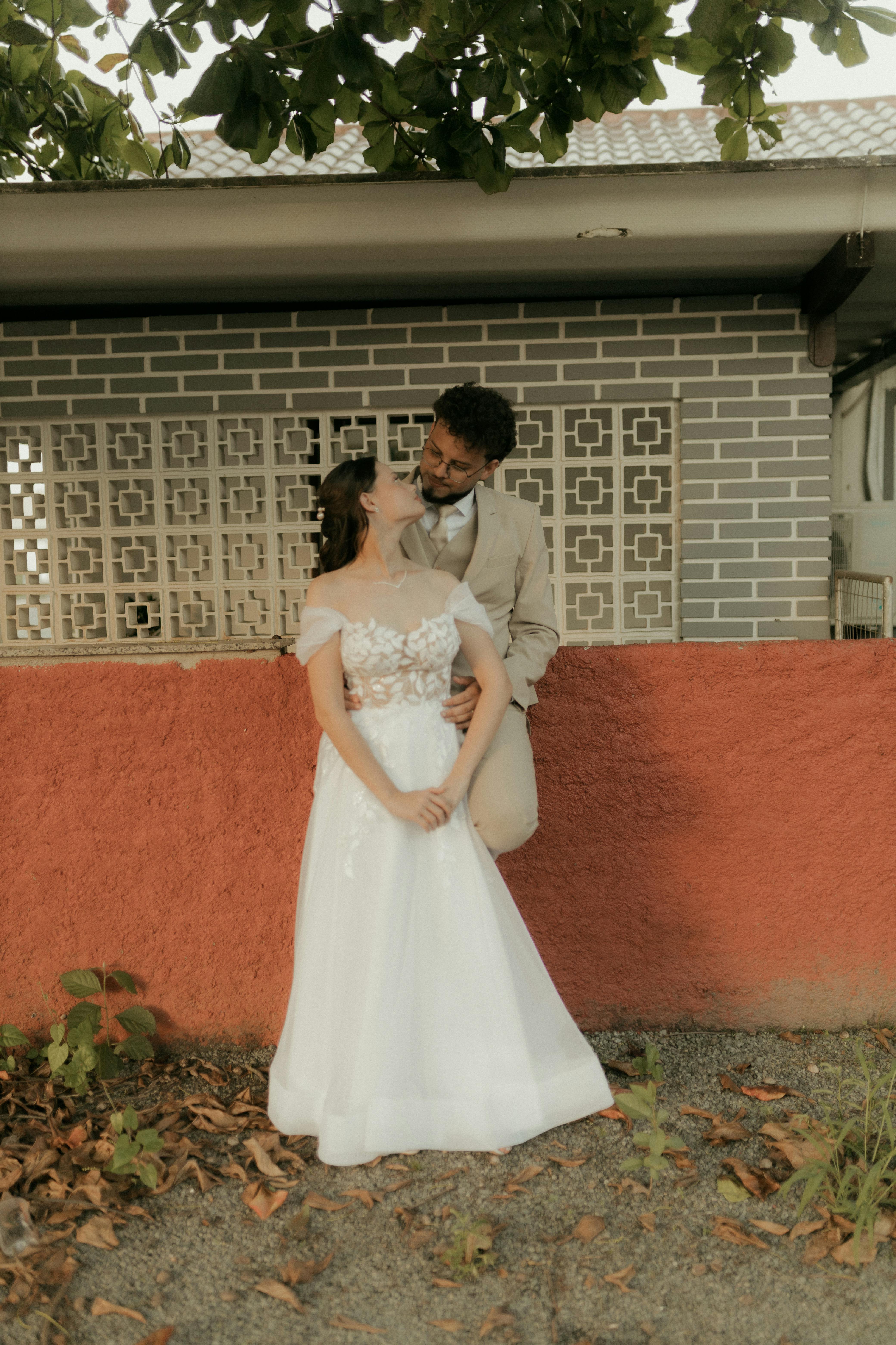 Gratuit Un couple marié, rayonnant de bonheur, s'enlace devant un mur coloré à l'extérieur, entouré d'un paysage naturel. Photos