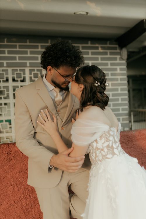 Free A loving couple in wedding attire embraces warmly against a brick wall, capturing a romantic moment indoors. Stock Photo
