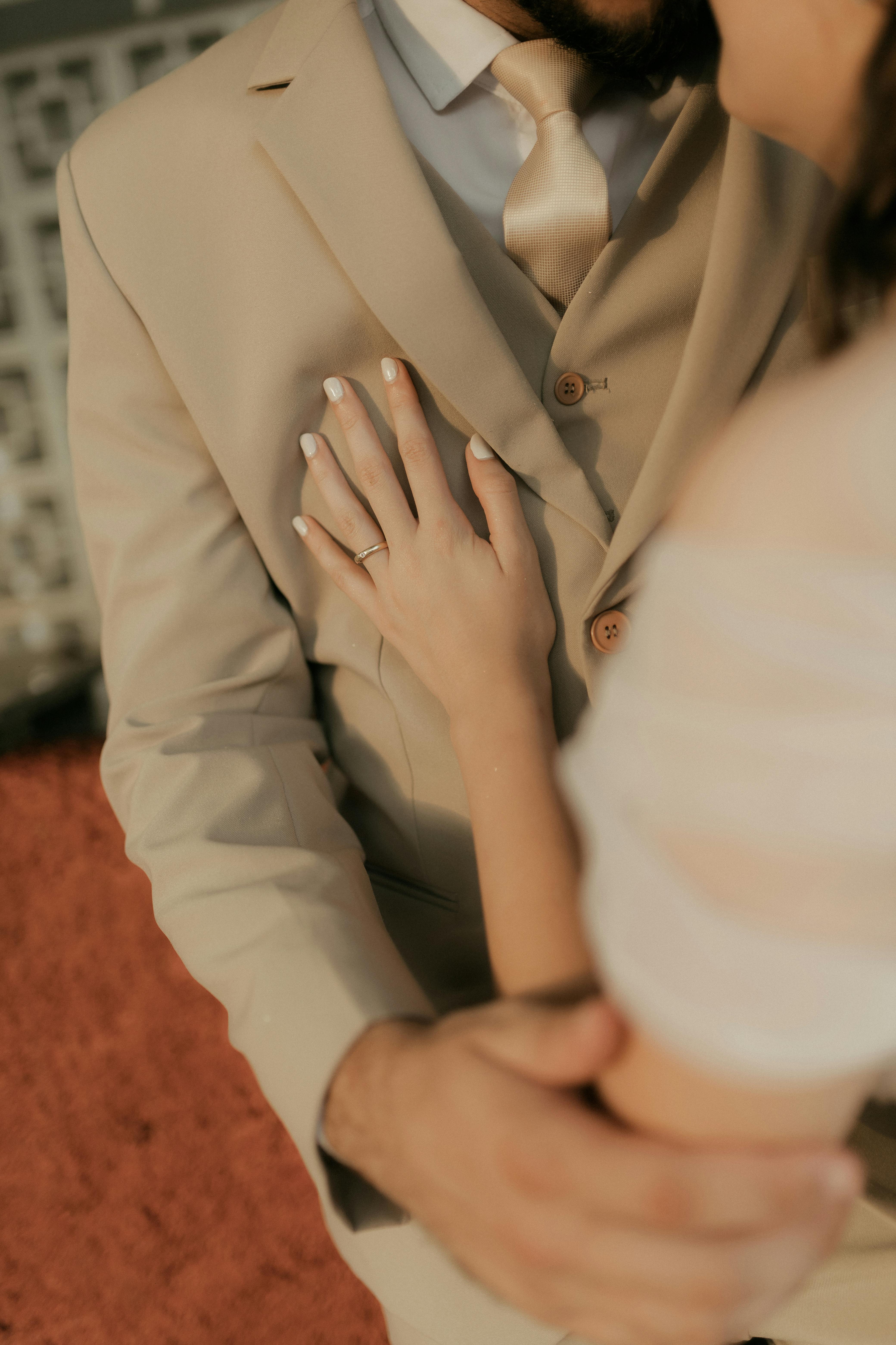 Gratuit Prim-plan al unui cuplu elegant îmbrățișat, concentrându-se pe mâini și costum bej. Moment cald și intim. Fotografie de stoc