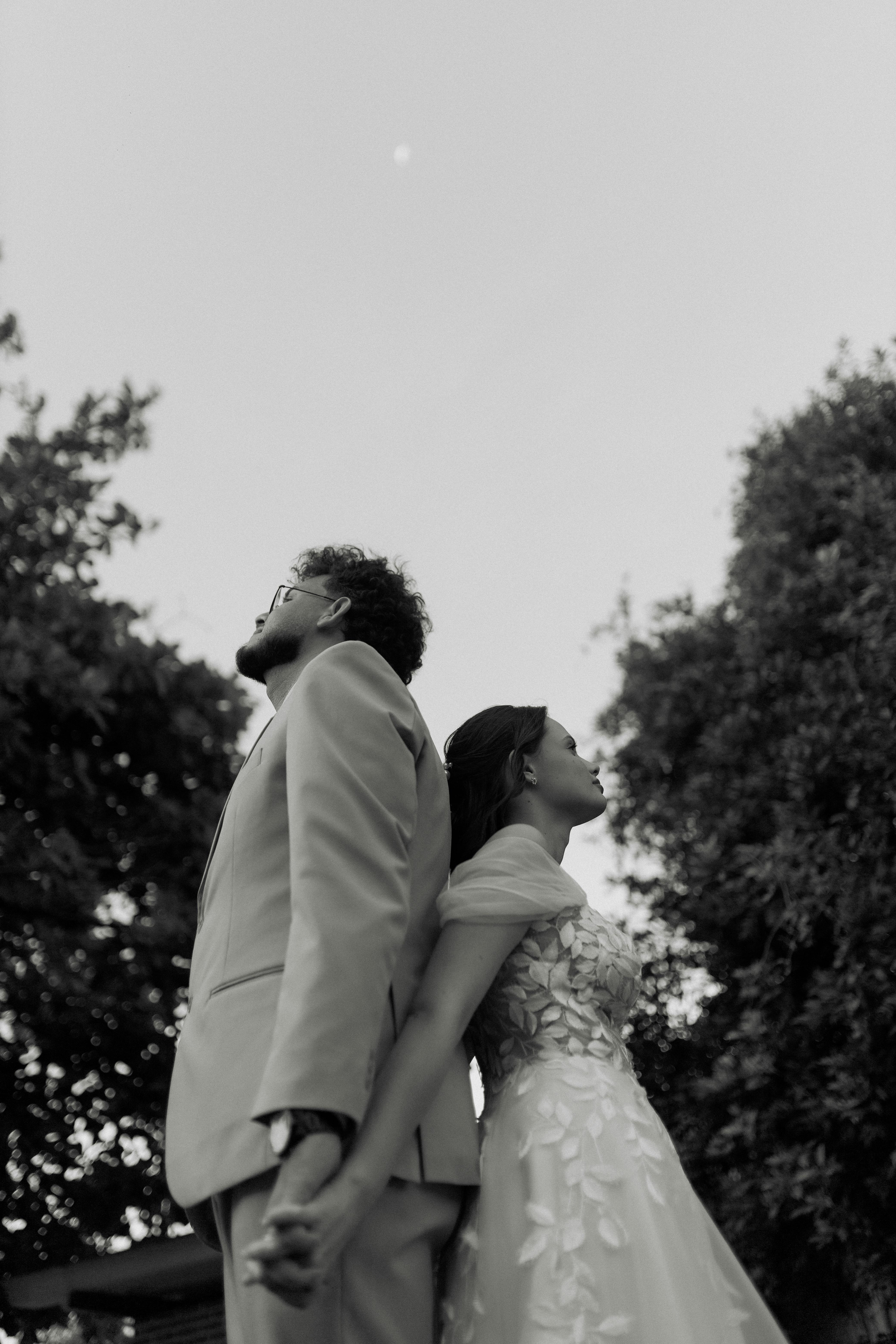 無料 屋外で背中合わせに立ち、手をつないでいるカップルを写した、ロマンチックなモノクロポートレート。 写真素材