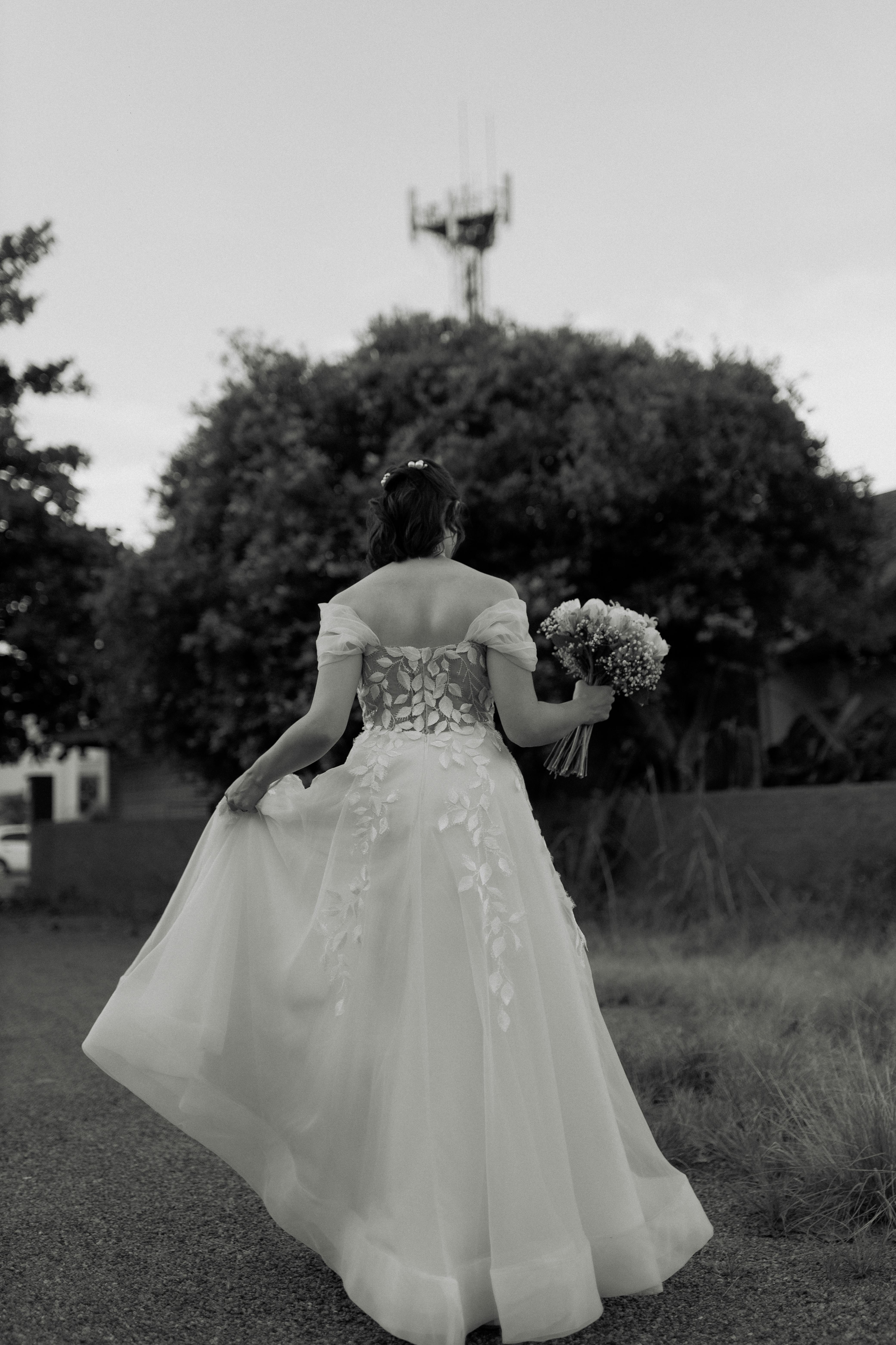 Kostnadsfria Elegant brud går utomhus i en vacker brudklänning som håller en bukett, fotograferad bakifrån. Stock foto