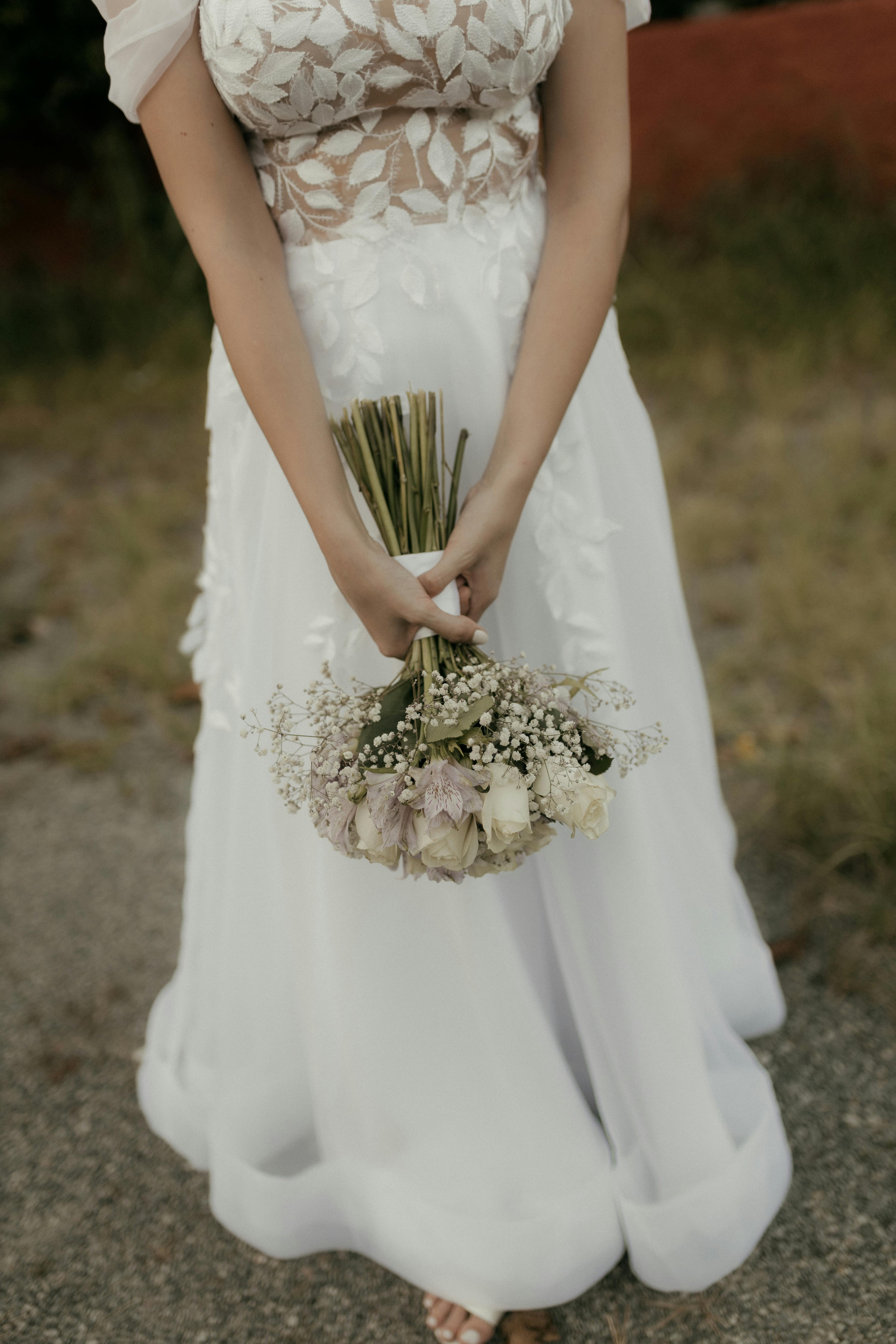 Kostenlos Nahaufnahme einer Braut, die im Freien einen weißen Blumenstrauß in einem zarten Brautkleid hält. Stock-Foto