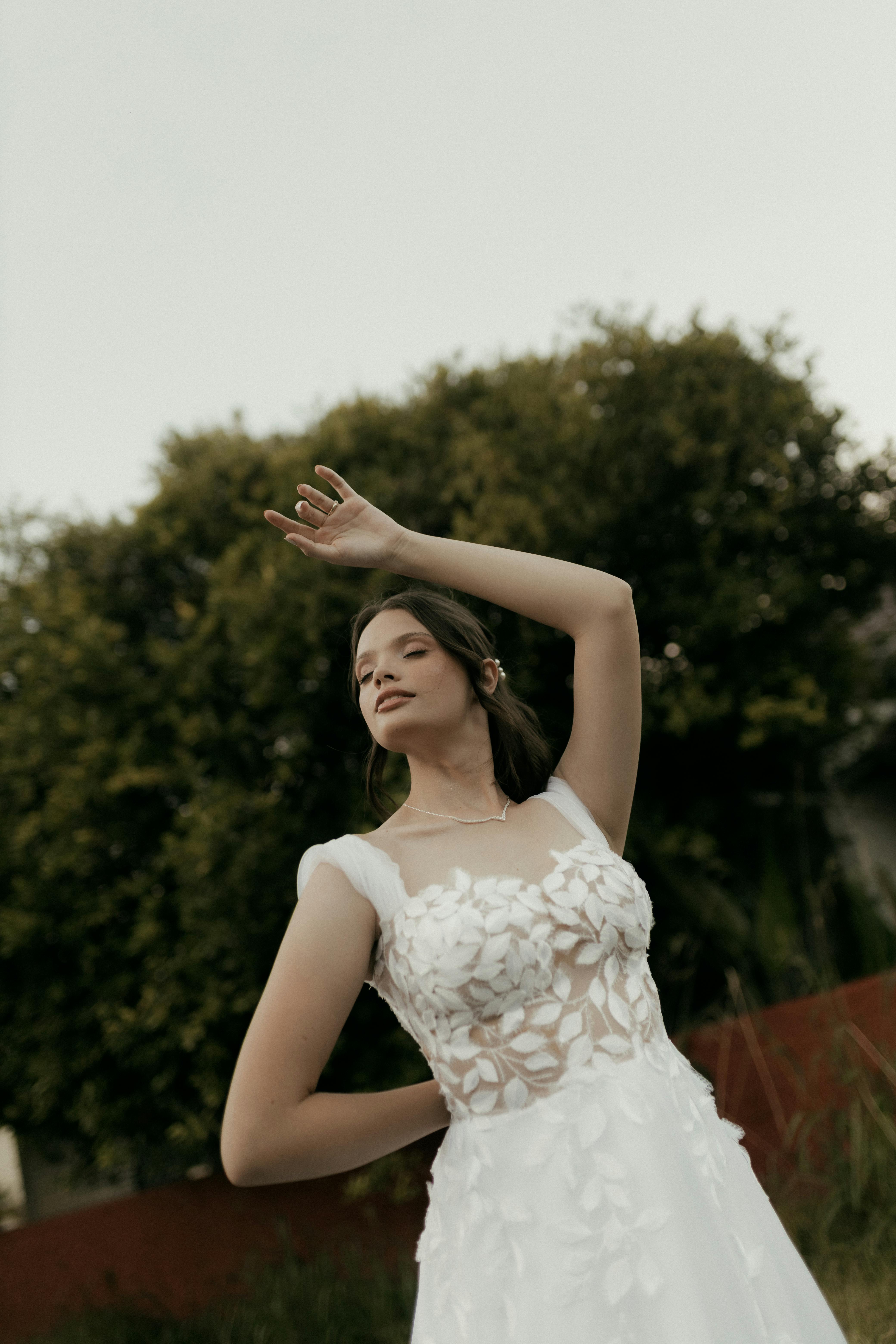 Gratuit Jeune mariée en robe de dentelle délicate posant gracieusement en extérieur, devant un décor de verdure luxuriante. Photos