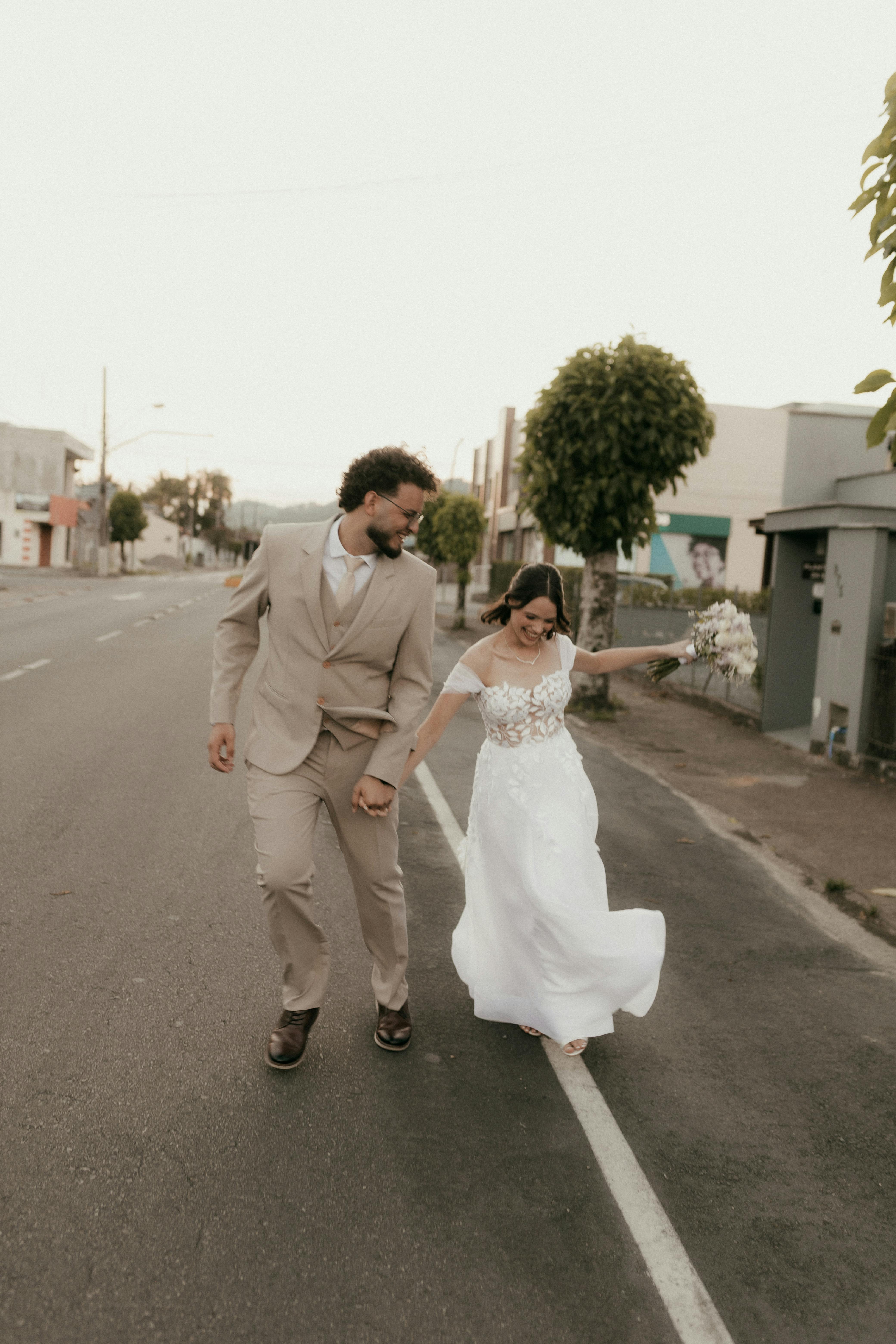 De franc Elegant parella de nuvis caminant alegremente per un carrer de la ciutat. Capturant l'amor i l'espontaneïtat en l'elegància urbana. Foto d'estoc