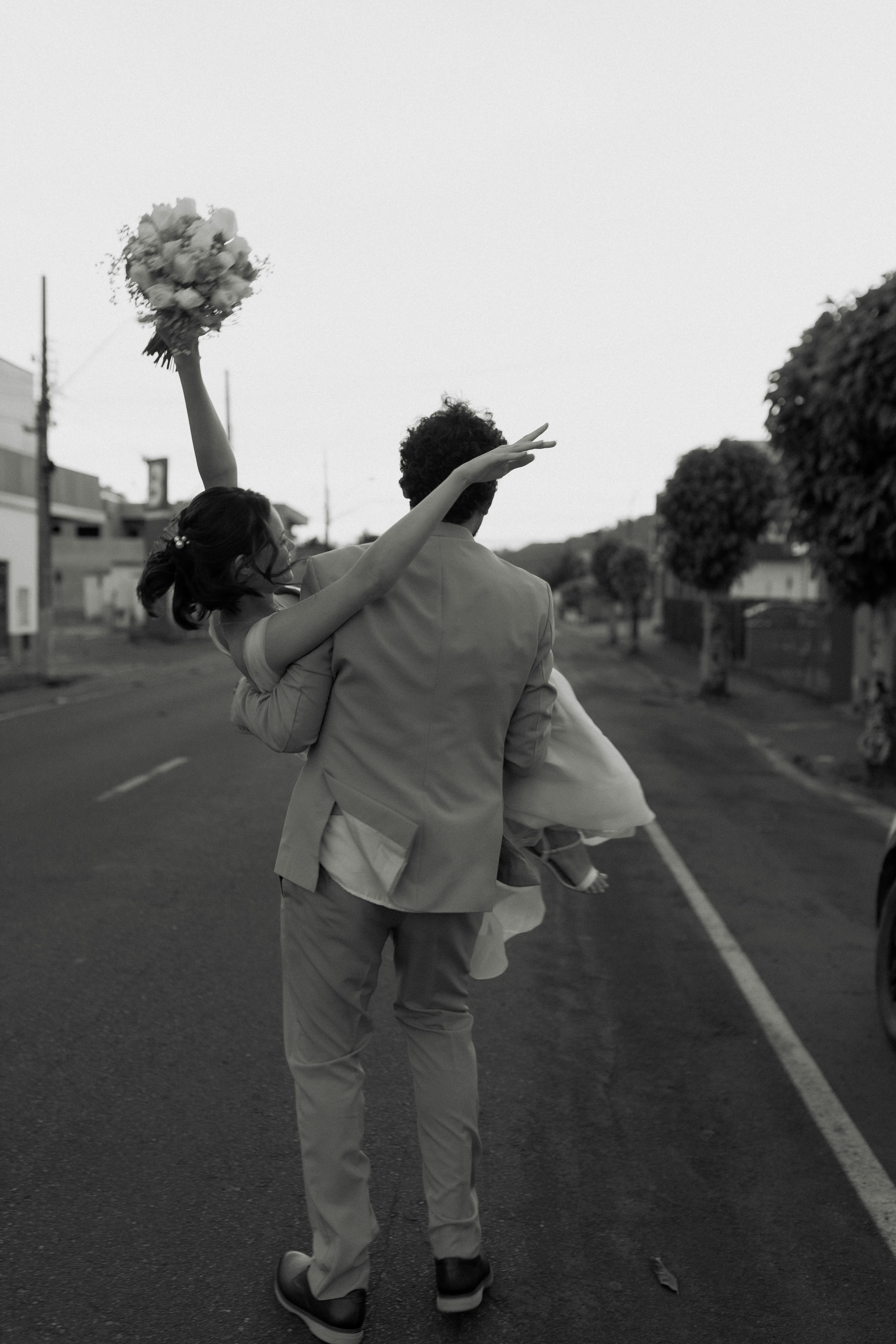 無料 新婚夫婦が都会の通りを喜びいっぱいに歩いている。花嫁はブーケを高く掲げている。 写真素材