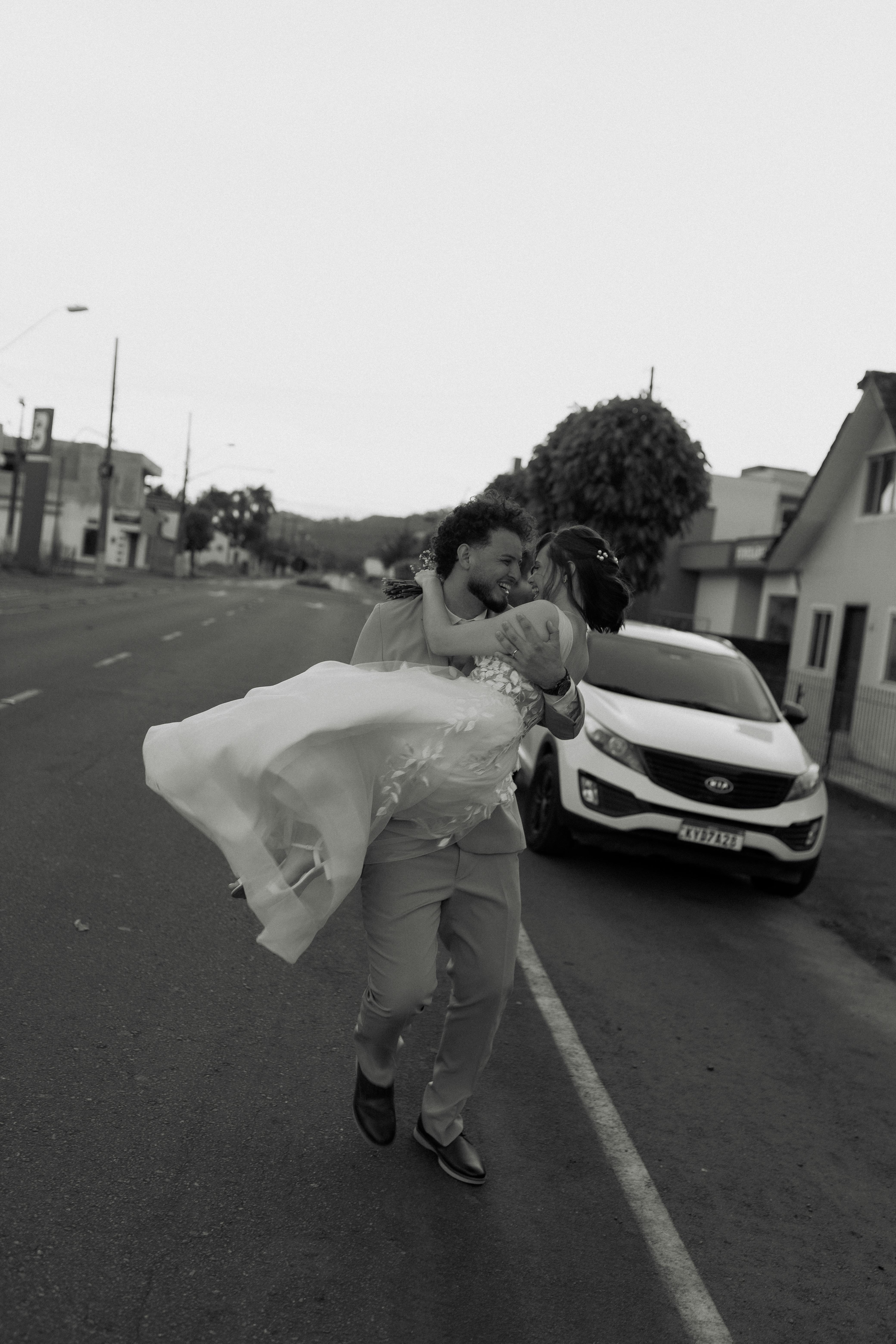 De franc Un nuvi porta la seva núvia alegrement per un carrer buit, capturant un moment intemporal del casament. Foto d'estoc