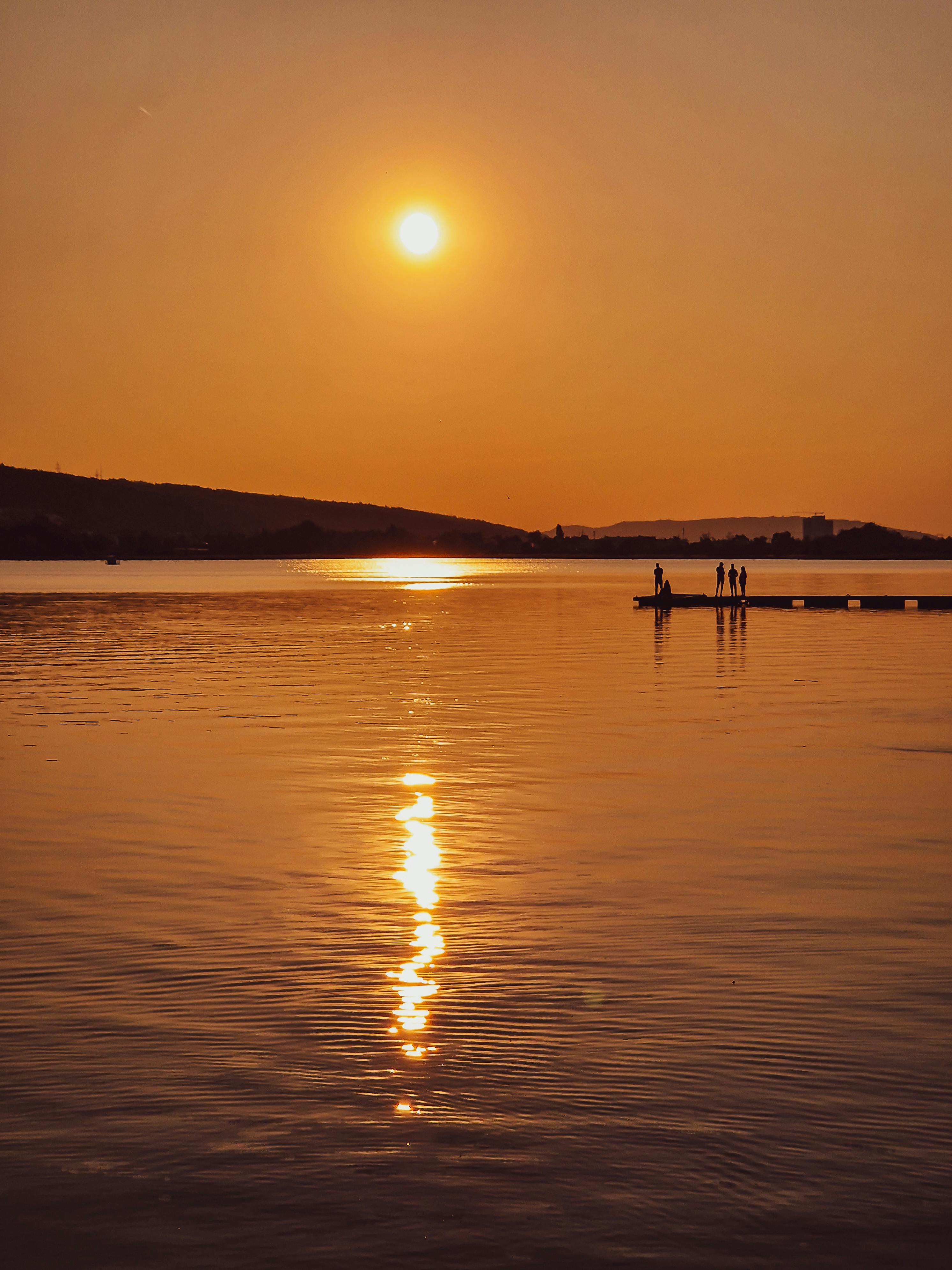 ฟรี พระอาทิตย์ตกดินเหนือทะเลสาบอันเงียบสงบ พร้อมเงาของคนในเงามืด คลังภาพถ่าย