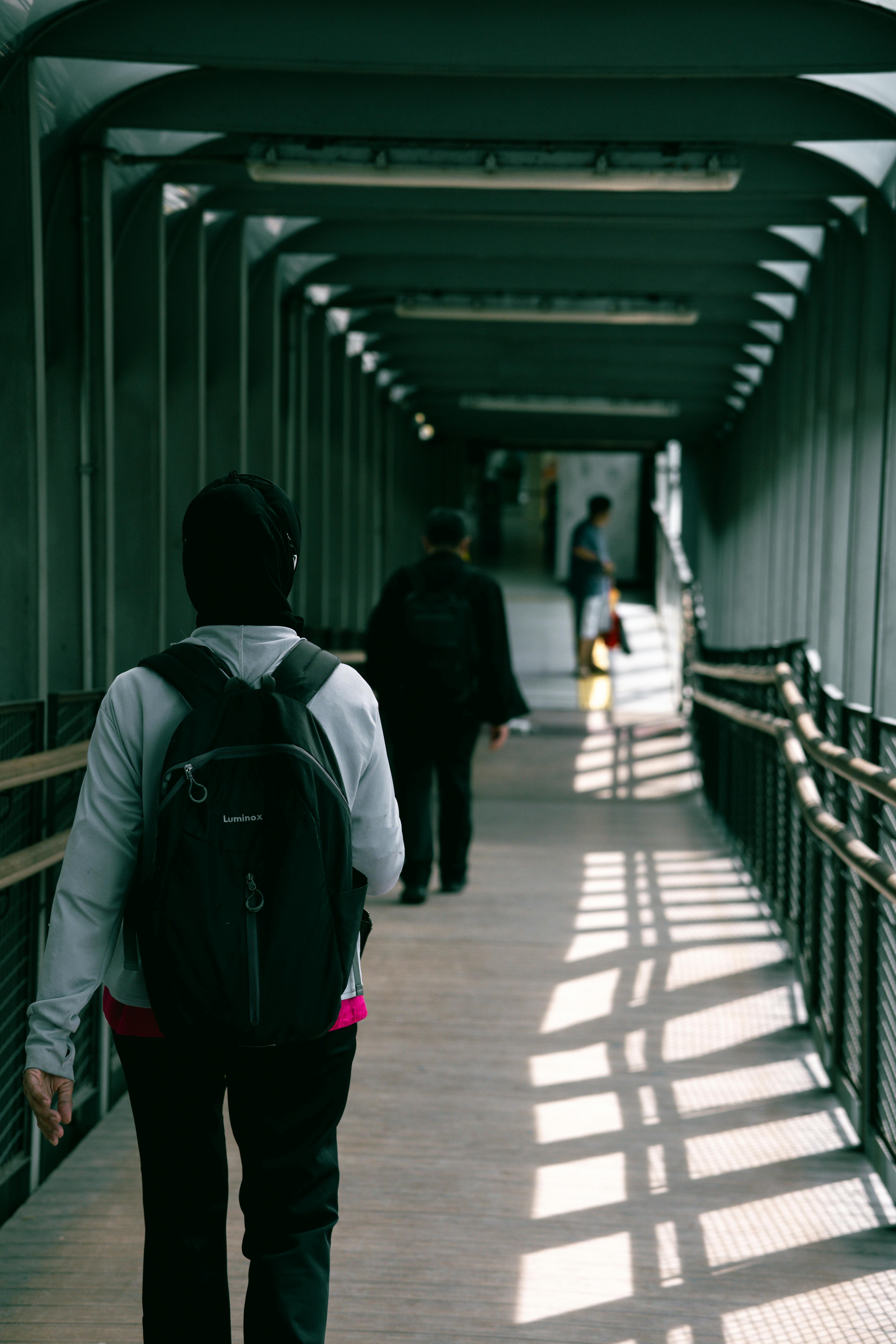 ingyenes Emberek kelnek át egy modern gyaloghídon, hosszú árnyékokat vetve a napfényben. Stockfotó