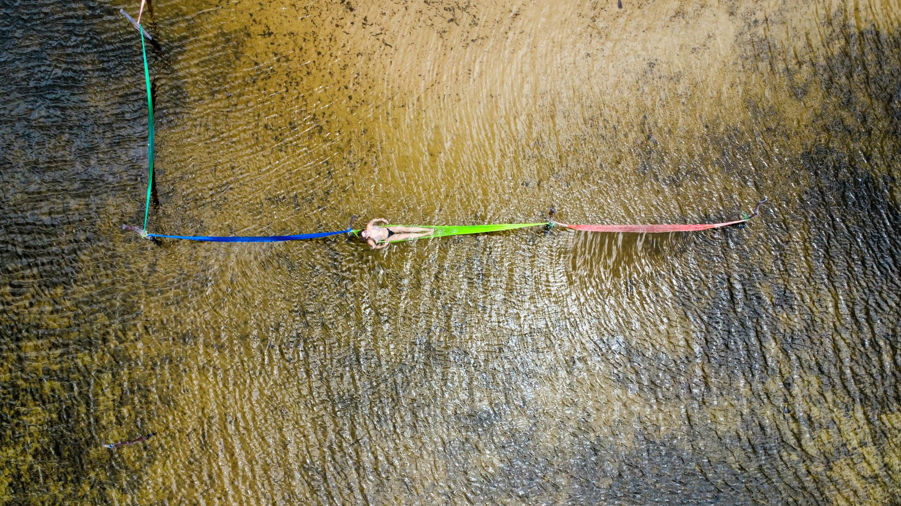 ingyenes Légifelvétel egy nőről, aki egy élénk színű függőágyban heverészik egy homokos folyómeder felett Natalban, Brazíliában. Stockfotó