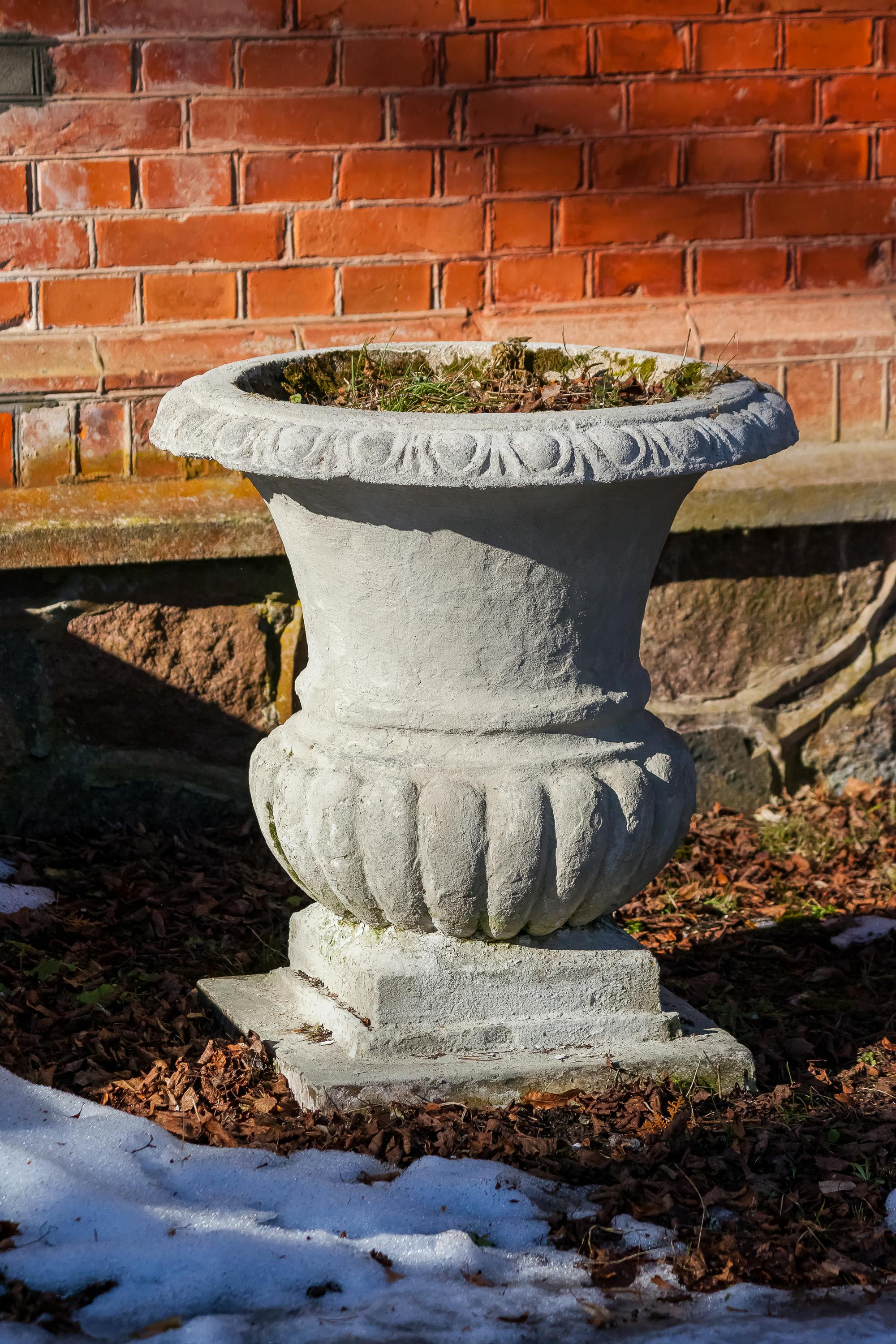 Miễn phí Chậu cây bằng đá trang nhã với những chiếc lá rụng, đặt dựa vào bức tường gạch dưới ánh sáng ban ngày, gợi lên hình ảnh mùa thu hoặc mùa đông. Ảnh lưu trữ