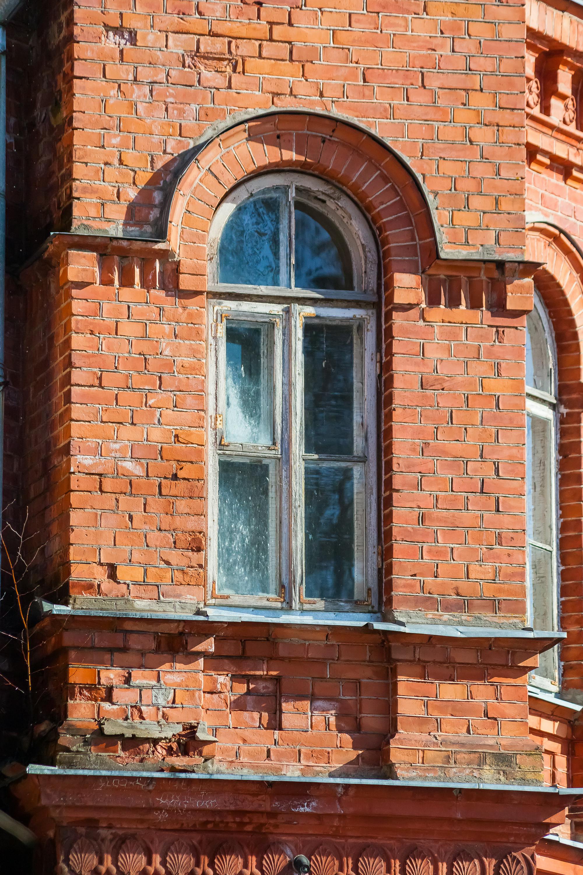 ingyenes Közeli kép egy régi téglaépület homlokzatáról, melyen egy boltíves ablak látható nappali fényben. Stockfotó