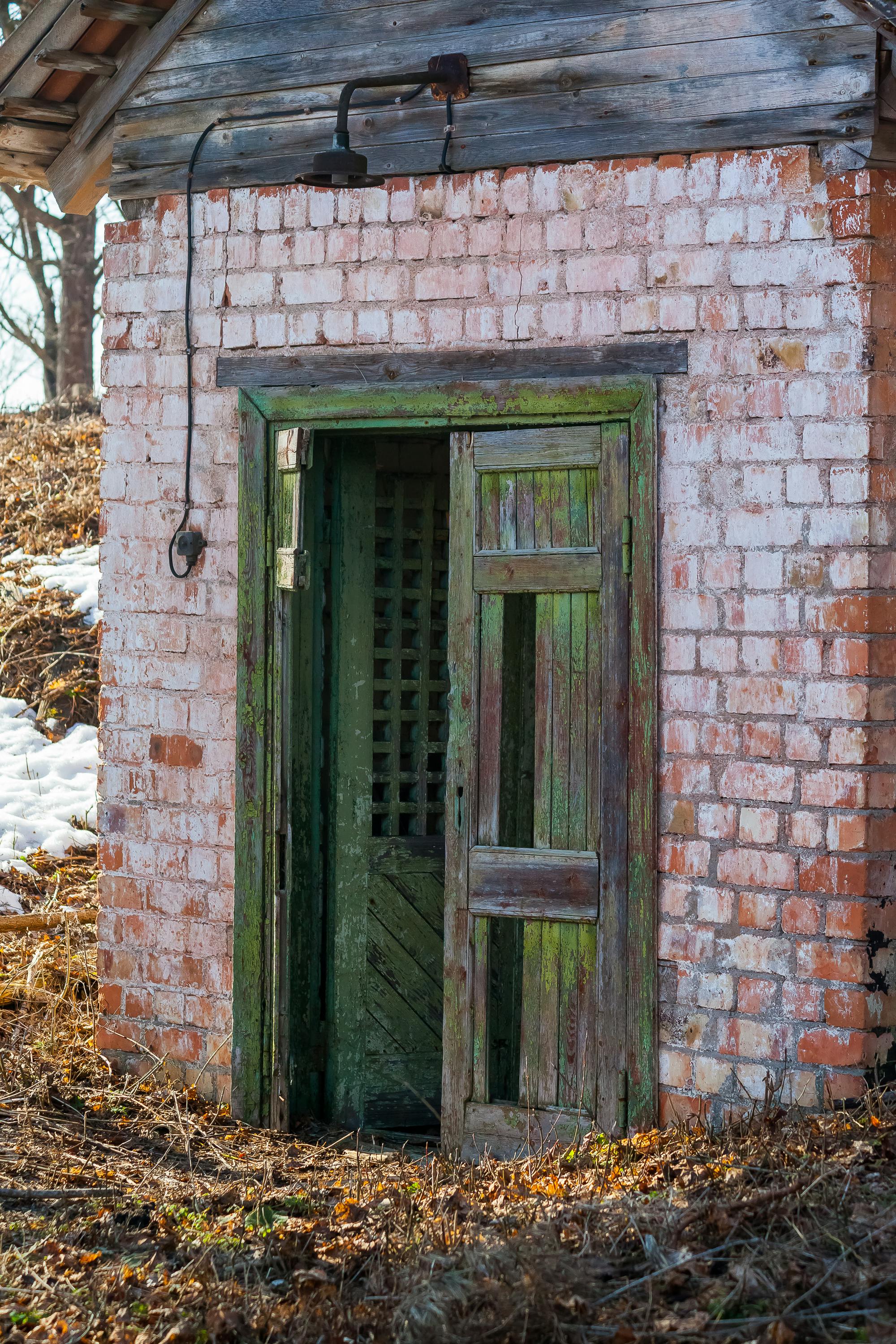무료 자연에 둘러싸인, 세월의 흔적이 묻어나는 녹색 나무 문이 낡은 벽돌 구조물에 자리 잡고 있다. 스톡 사진