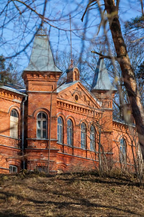 Free Old red brick building with spires in a wooded area, creating a vintage atmosphere. Stock Photo