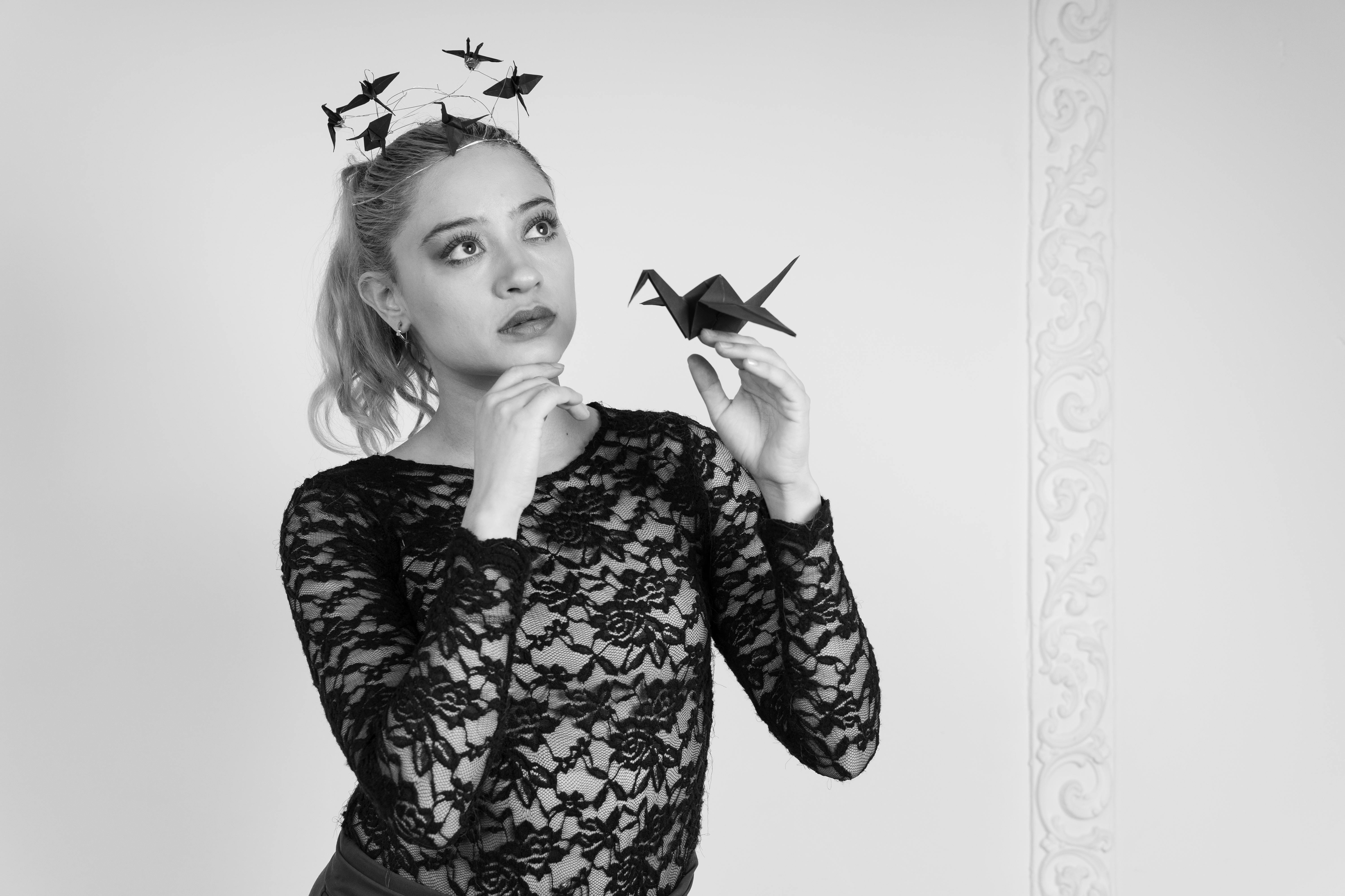 免费 一位身着黑色蕾丝的优雅女子手捧一只折纸鹤，举手投足间流露出优雅与沉思。 素材图片