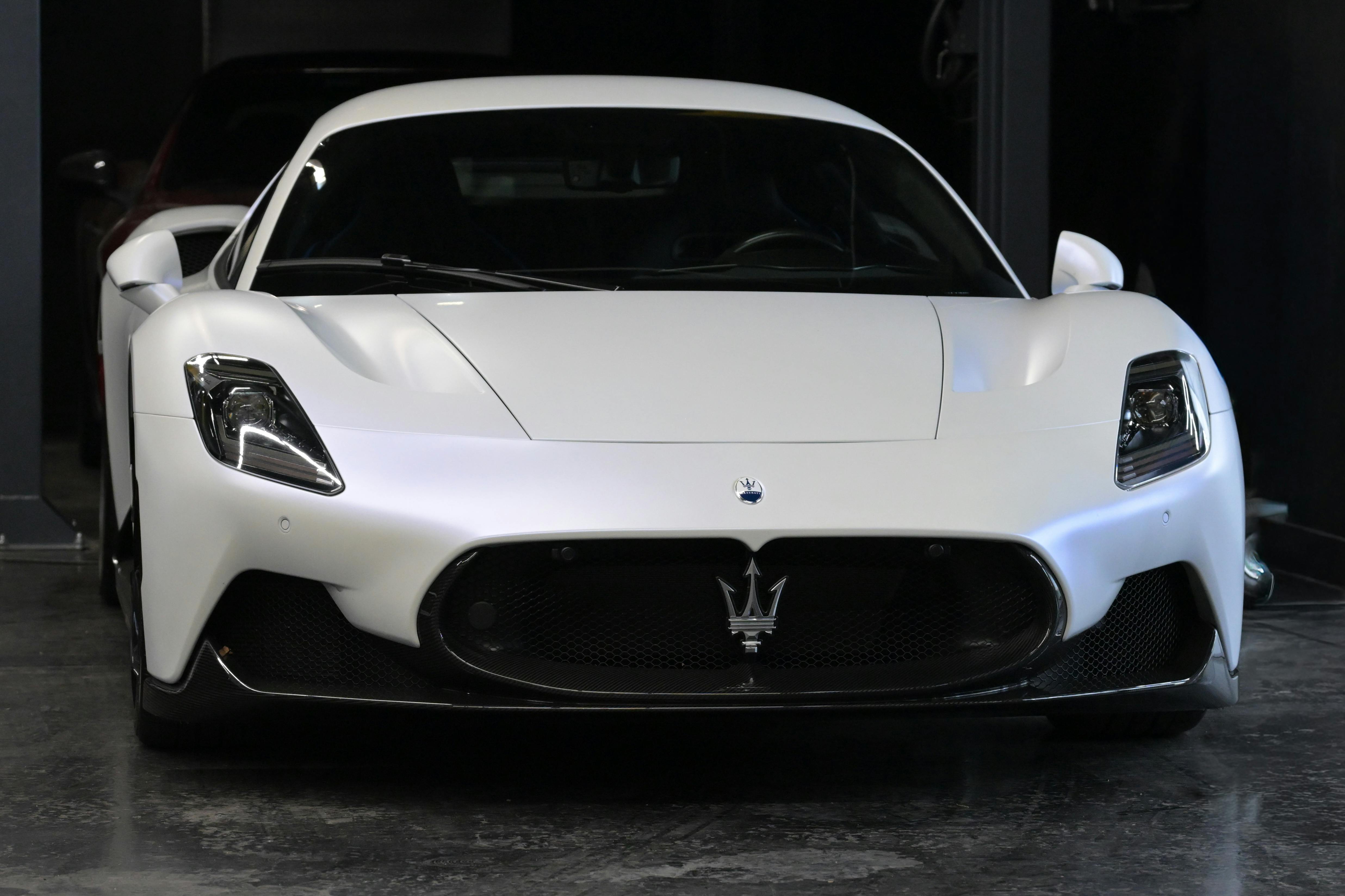 Free Front view of a striking white Maserati supercar showcased in a dimly lit garage setting. Stock Photo