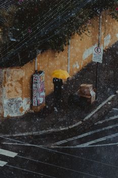 A rainy street scene with a person under a yellow umbrella, adding vibrant contrast to the urban landscape.