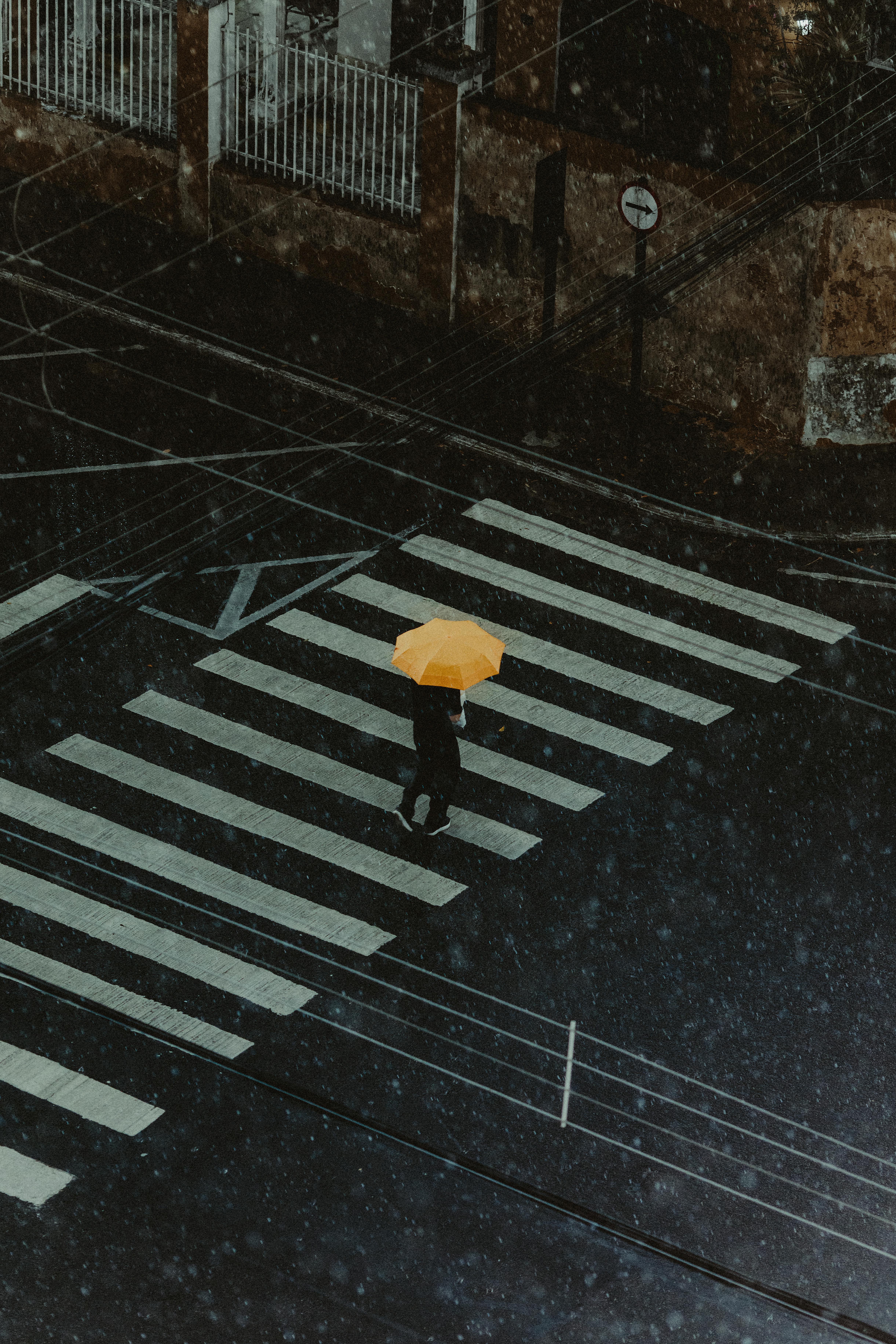 Безкоштовне Людина з жовтою парасолькою перетинає міську вулицю під дощем, видно згори. стокове фото