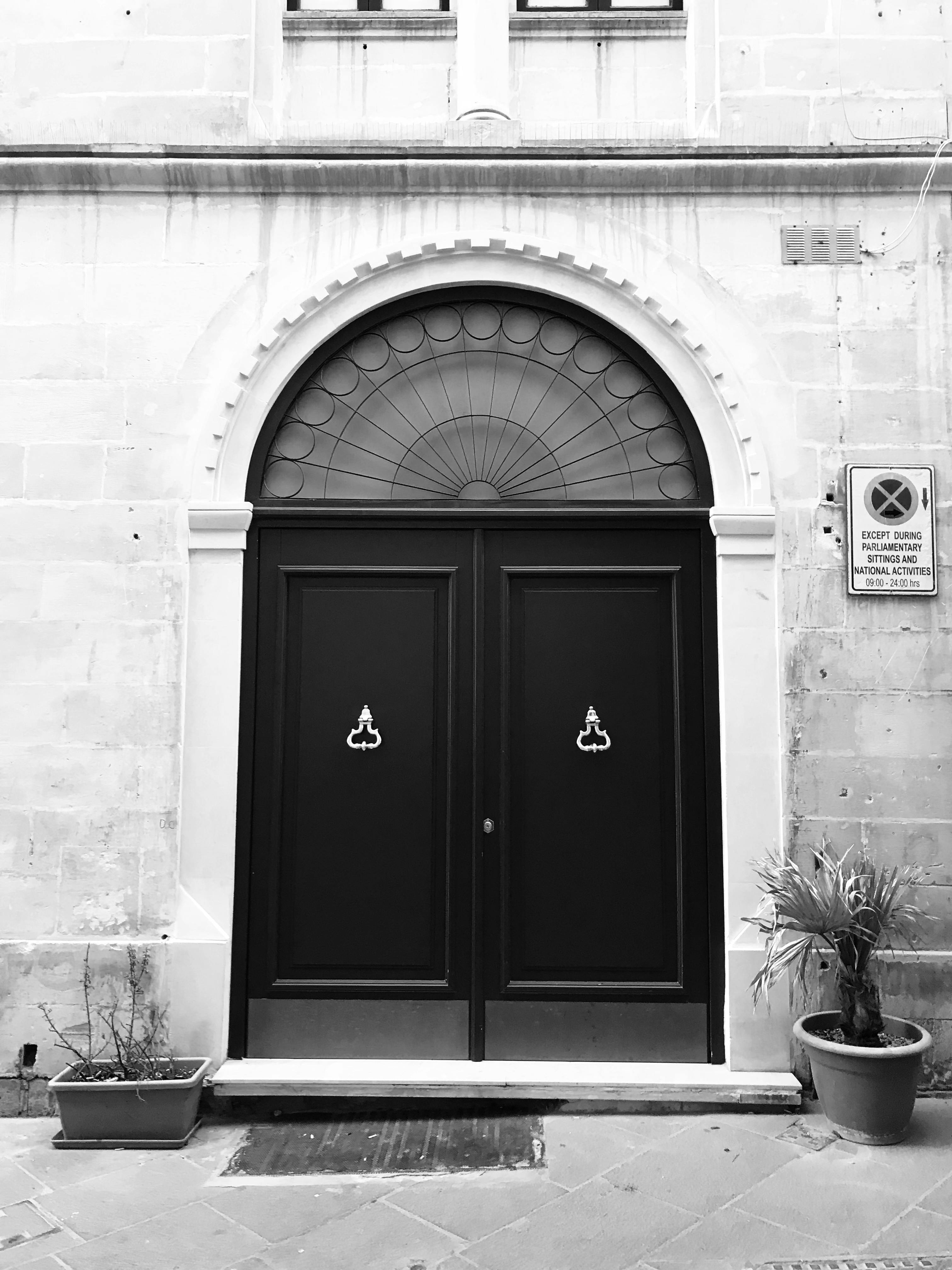 Zadarmo Čierne dvojkrídlové dvere v historickej kamennej fasáde s črepníkovými rastlinami. Fotka z fotobanky