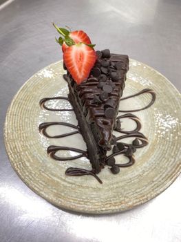 A rich chocolate cake slice topped with a fresh strawberry and chocolate chips, elegantly presented.