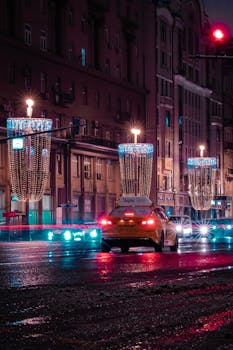City street at night with festive lights and cars in the rain, providing a vibrant urban scene.