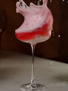 High-speed capture of a pink-red cocktail splashing in a tall glass on a marble surface.