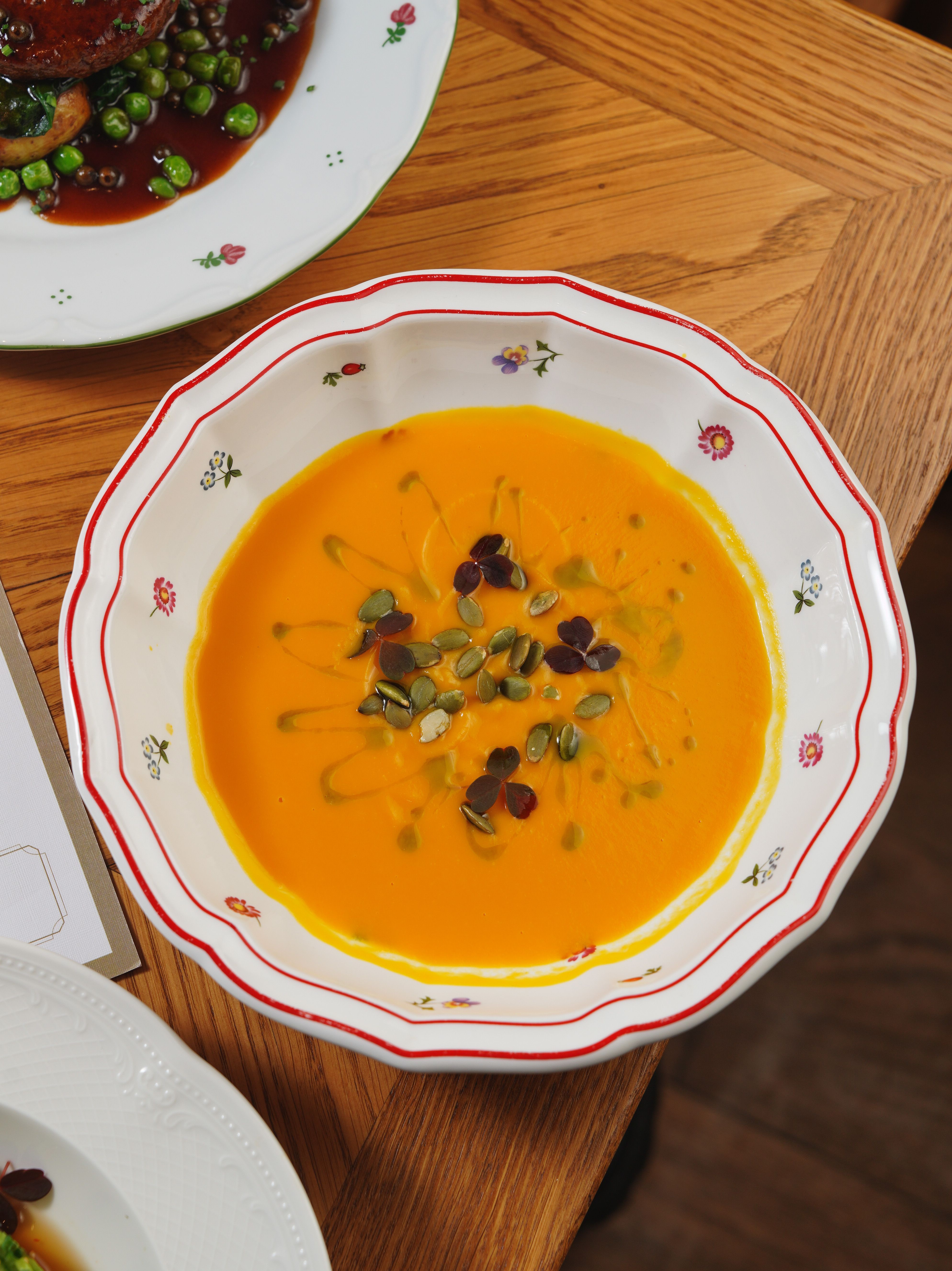 Delicious homemade pumpkin soup garnished with seeds and microgreens in a floral-patterned bowl.