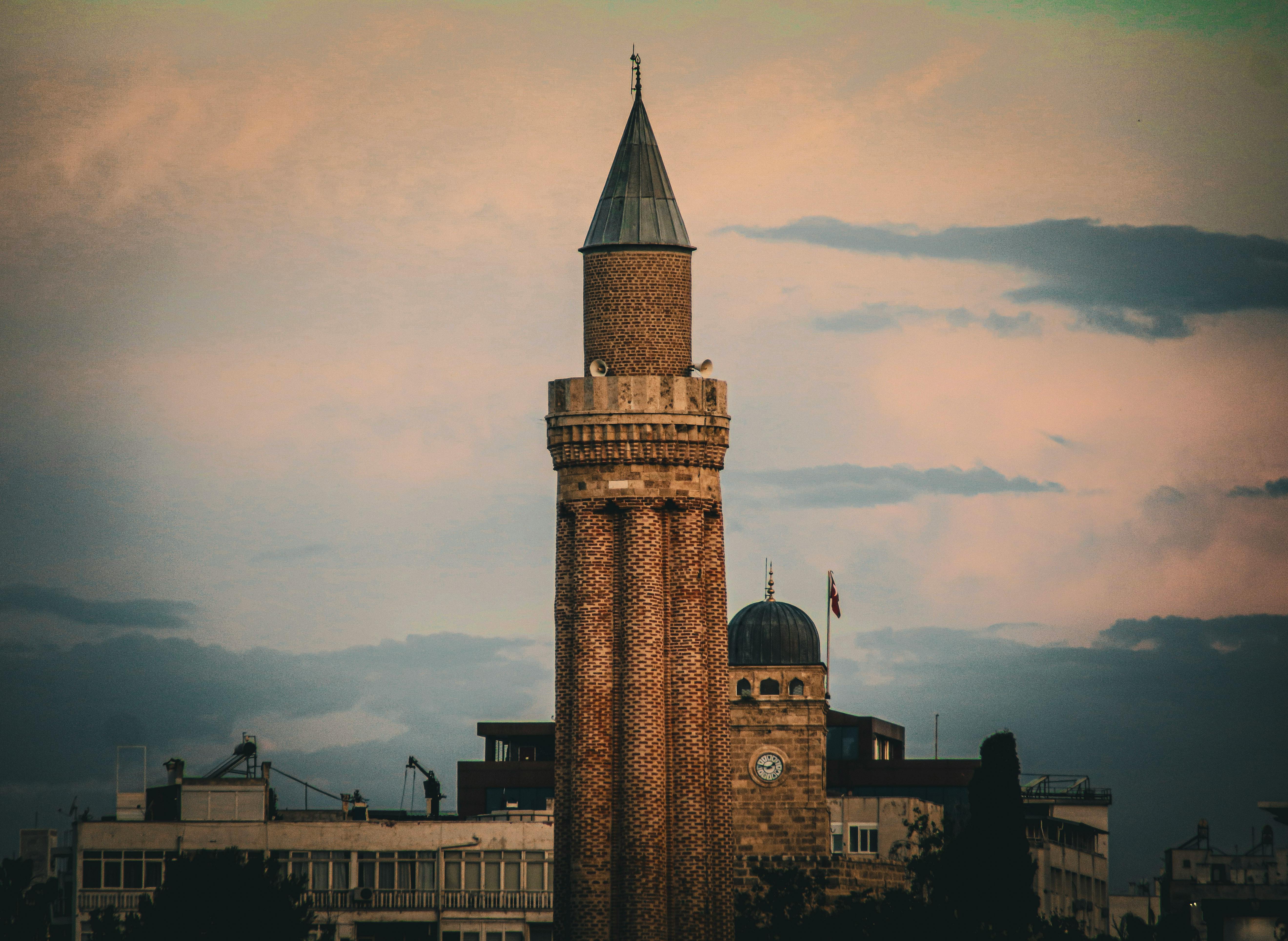 ฟรี หอคอยมัสยิดเก่าแก่ตั้งตระหง่านอยู่เบื้องหน้าท้องฟ้ายามเย็นอันงดงาม สะท้อนความสง่างามทางวัฒนธรรม คลังภาพถ่าย