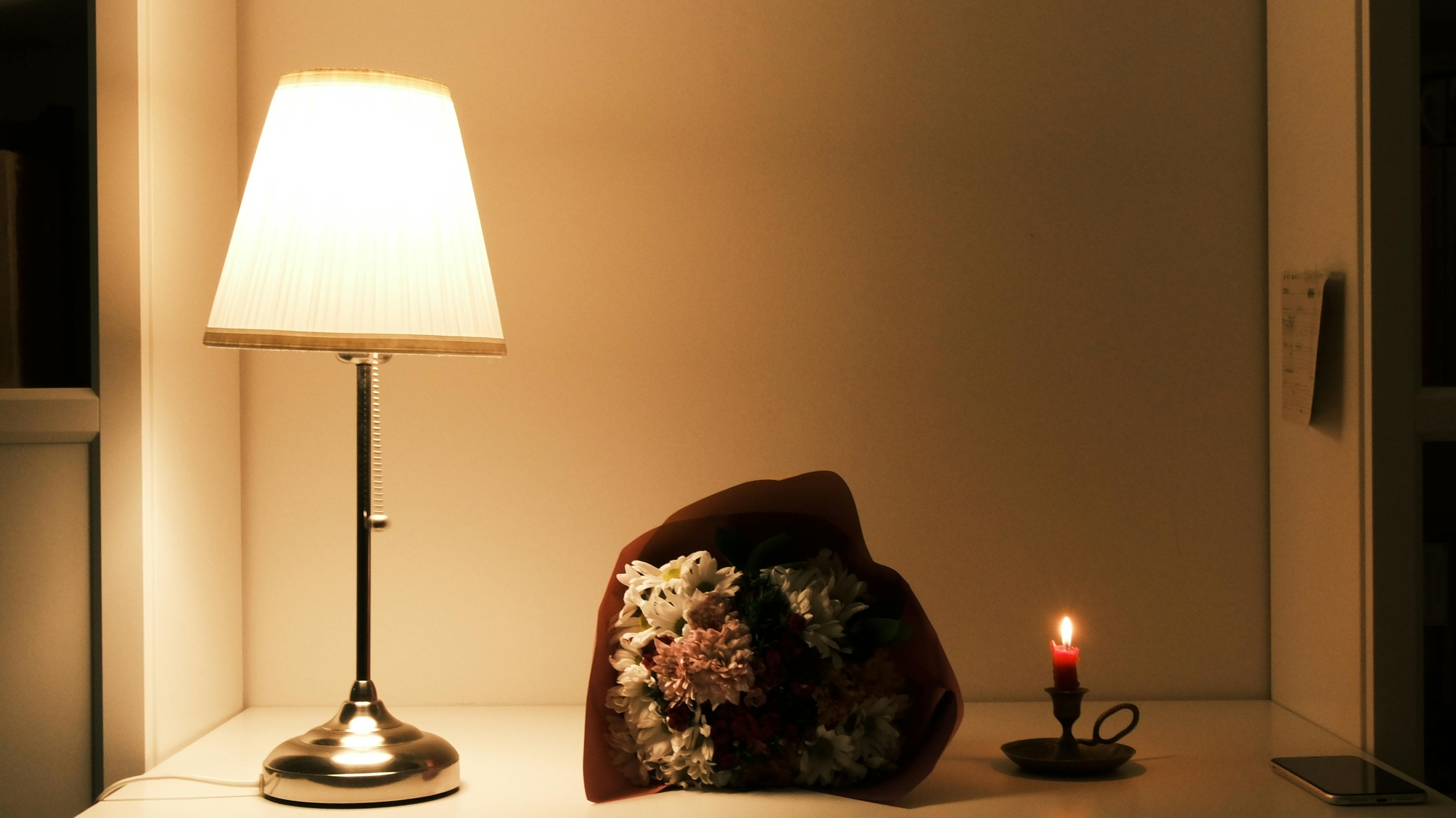 Kostenlos Gemütliches Ambiente mit einer Tischlampe, einem Blumenstrauß und einer brennenden Kerze auf dem Tisch. Stock-Foto