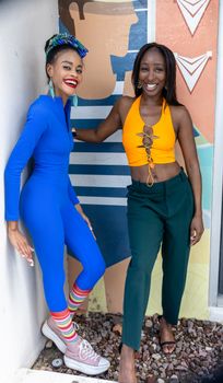 Two women in vibrant outfits showcase trendy urban fashion against a mural backdrop.