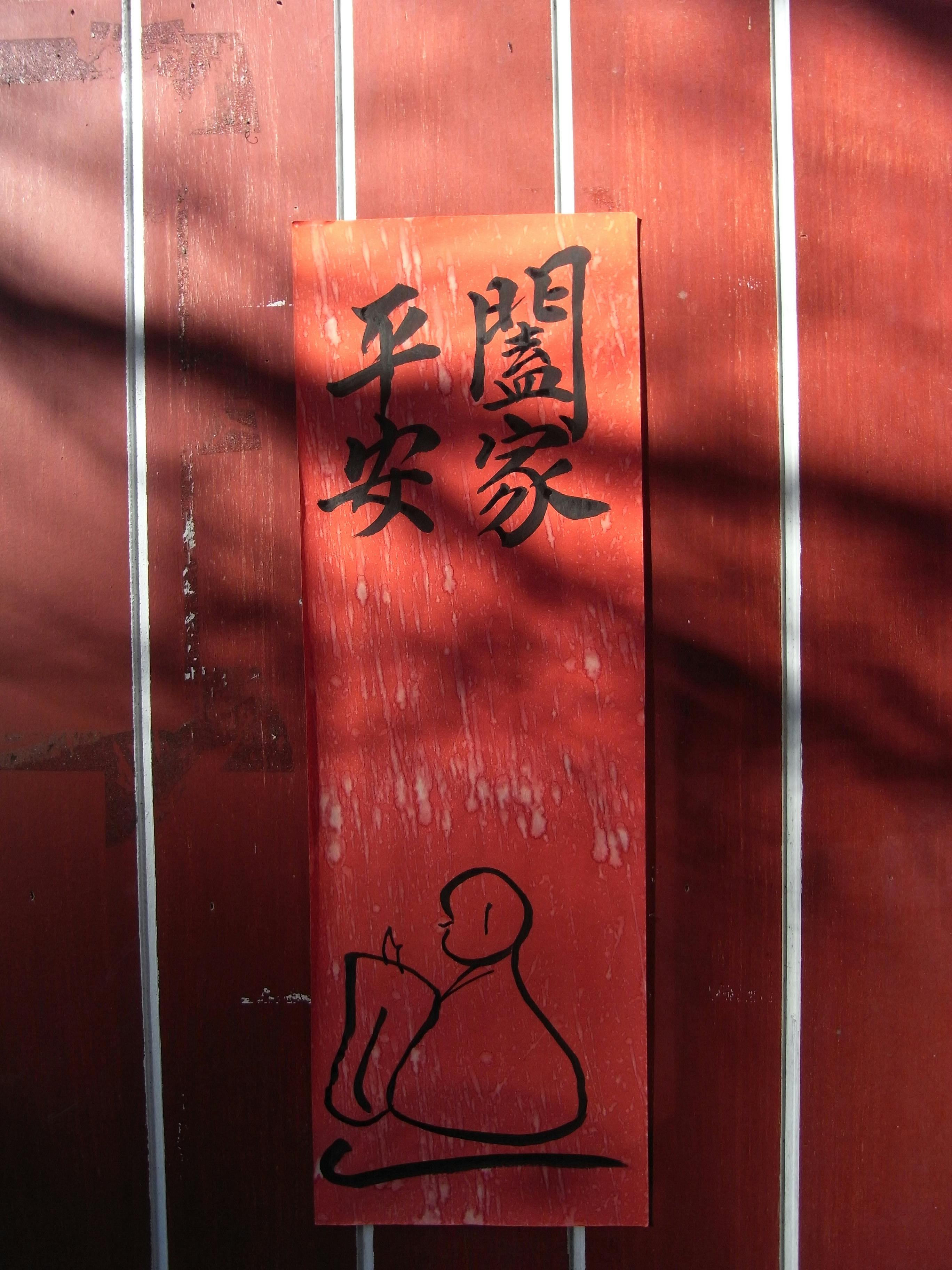 Kostenlos Eine strukturierte rote Wand mit einem vertikalen Schild, das chinesische Kalligrafie und Schattenspiele zeigt. Stock-Foto