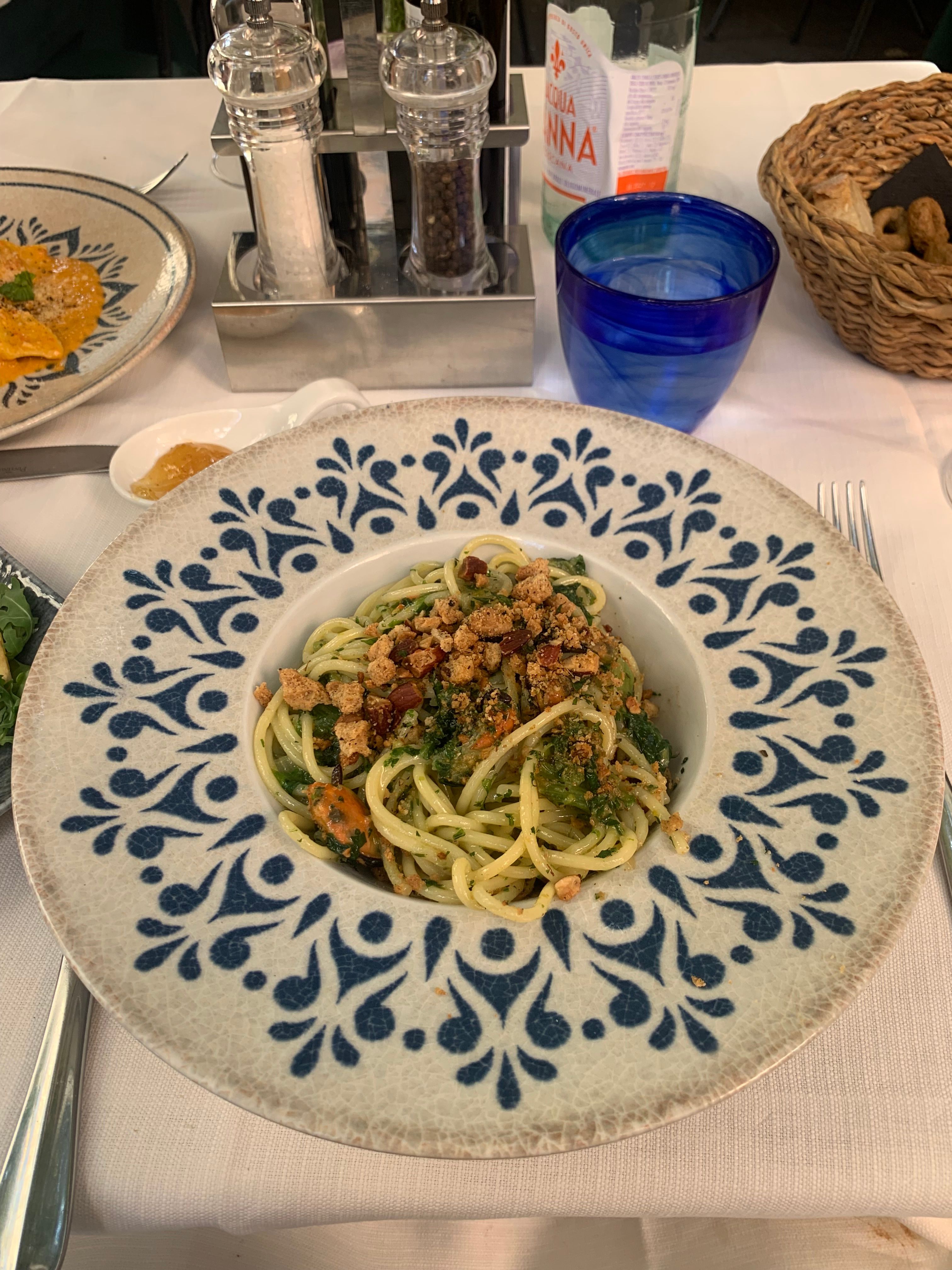 A plate of spaghetti with herbs and croutons served on a decorative table setting.