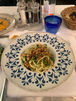 A plate of spaghetti with herbs and croutons served on a decorative table setting.