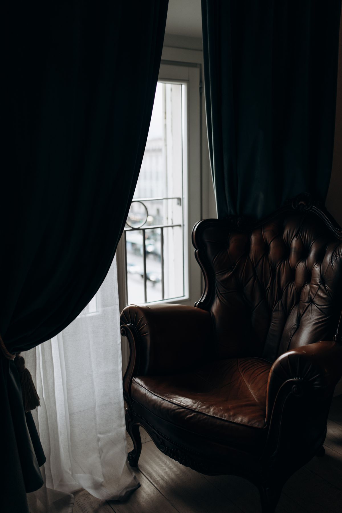 A worn vintage leather armchair set beside a curtained window, a ready-made reading corner for short winter afternoons
