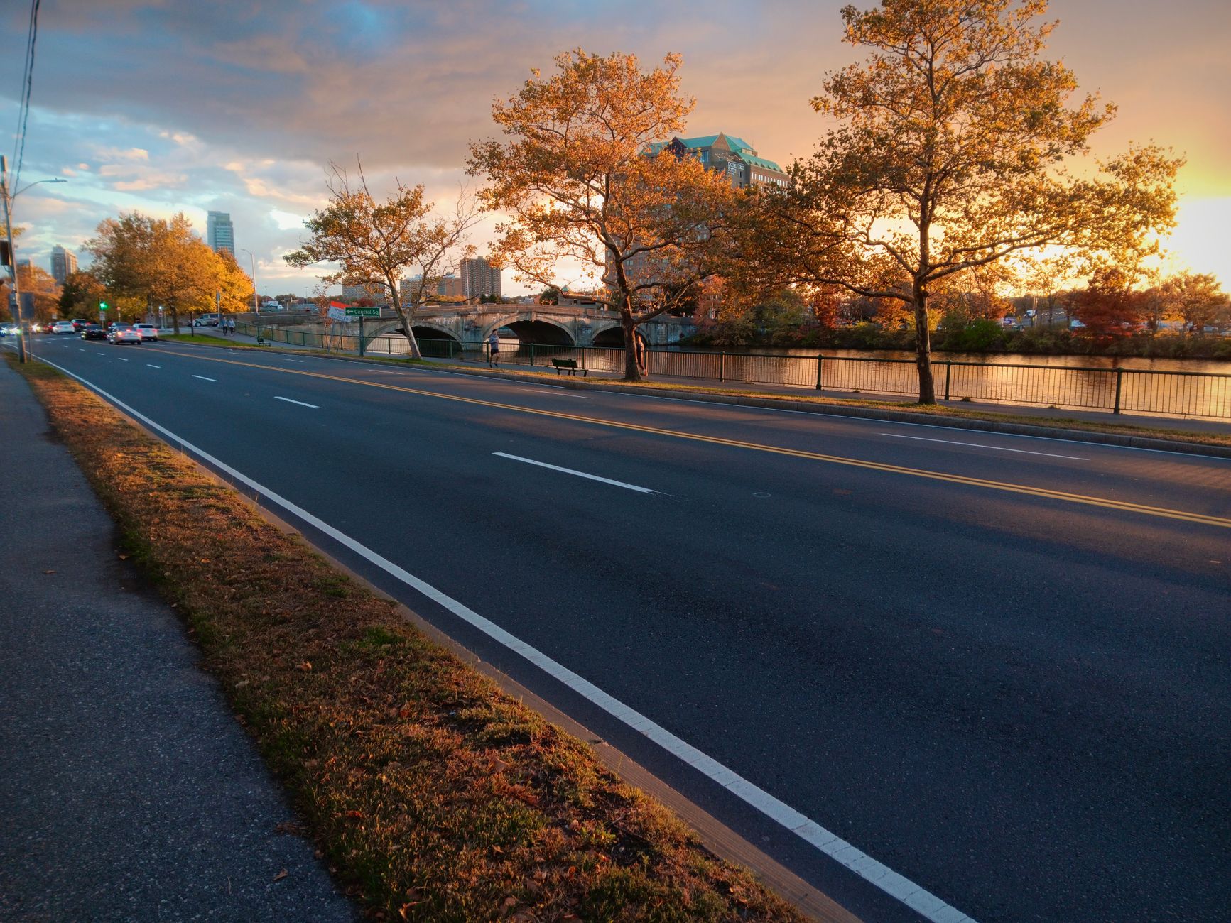 A serene sunset view of an empty road lined with autumn trees beside a river.
