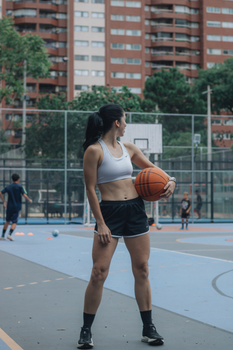 Athletic woman stands confidently with basketball on outdoor court.